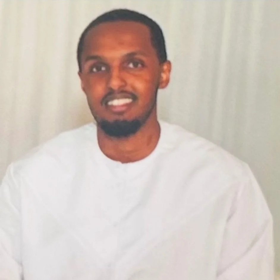 Nærbilde av en mann med kort hår og skjegg, iført en grå Nike sportsjakke, innendørs med takpanel i bakgrunnen.