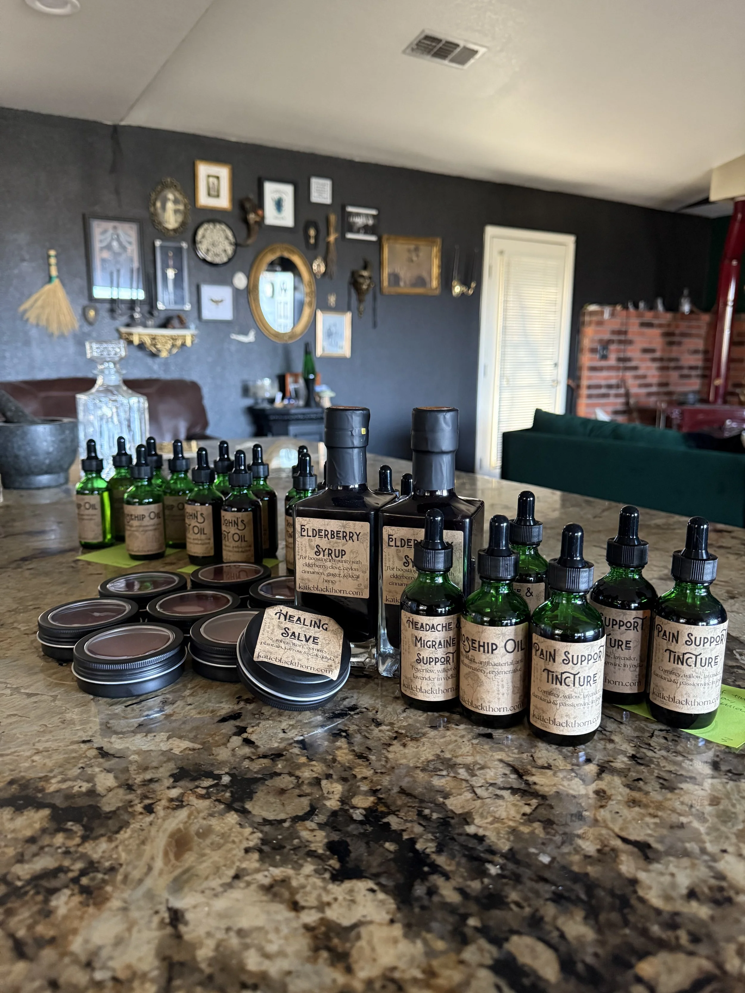 Collection of herbal tincture bottles and jars on a granite kitchen countertop, with a decorated wall in the background.