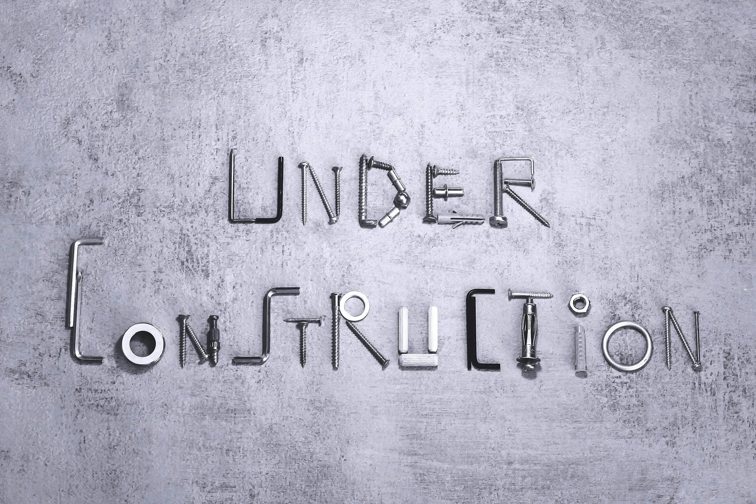 The words 'Under Construction' spelled out with various metal screws and nails on a concrete background.