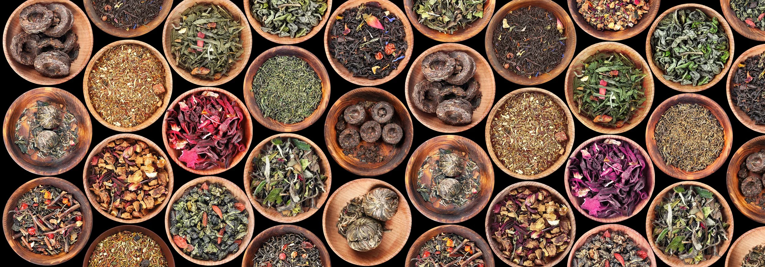 Various dried loose leaf teas in small wooden bowls on a black background.