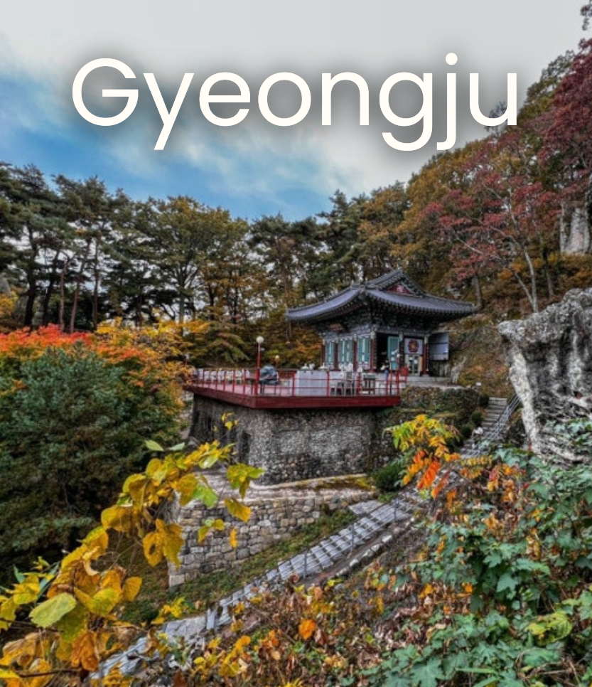 A scenic view of Gyeongju, South Korea, featuring traditional Korean architecture on a hillside with colorful autumn foliage and a cloudy sky.