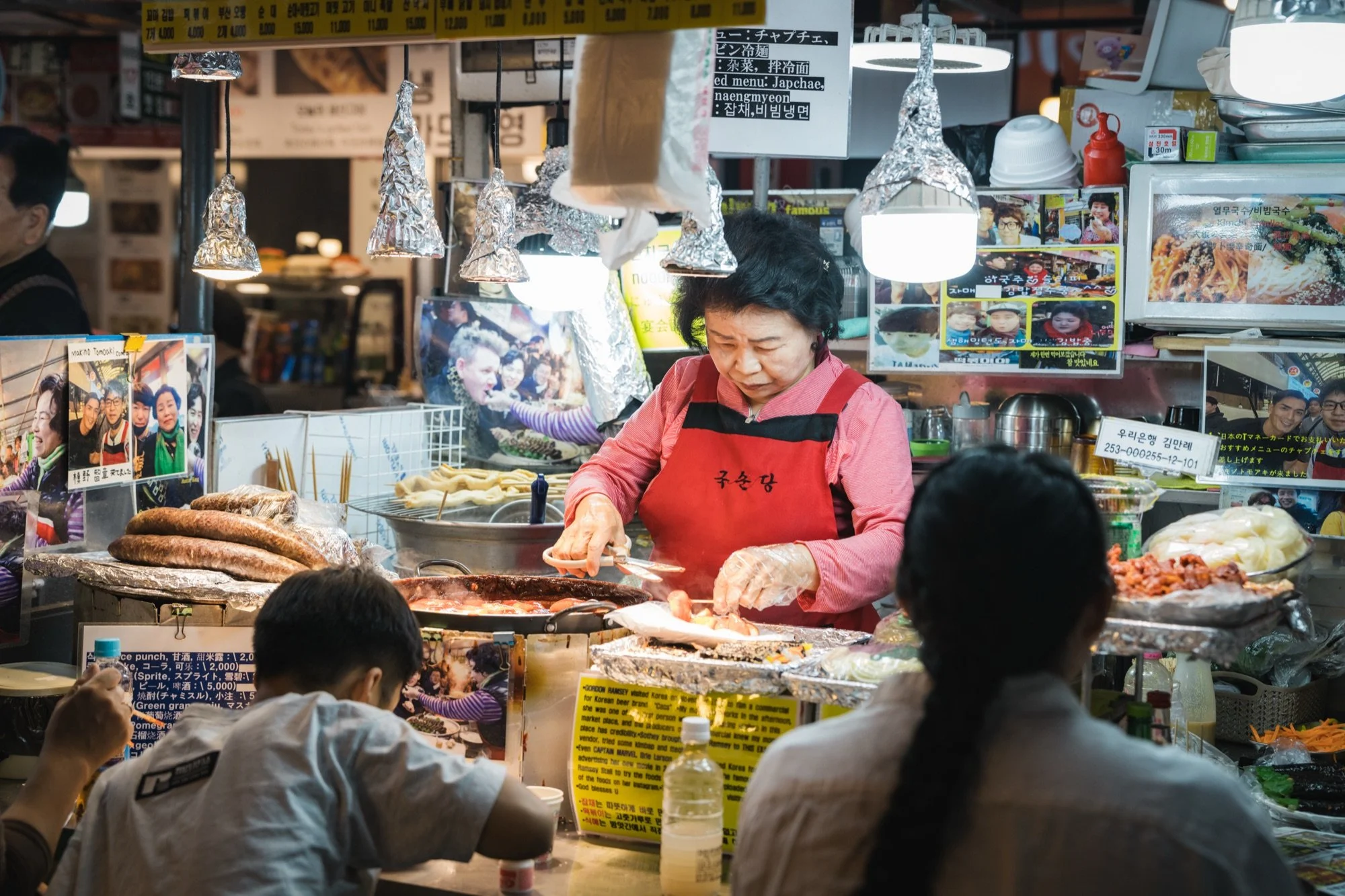 A vendor cooking at a busy market food stall in Seoul while customers wait