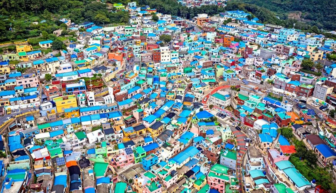 Aerial view of a colorful hillside neighborhood with houses painted in various bright colors, narrow streets winding through the area, surrounded by green trees and hills.