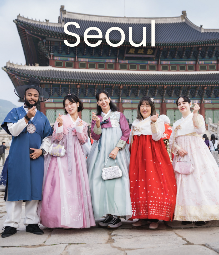 Group of five people in traditional Korean hanbok standing in front of Gyeongbokgung Palace in Seoul, South Korea, smiling and posing for a photo.