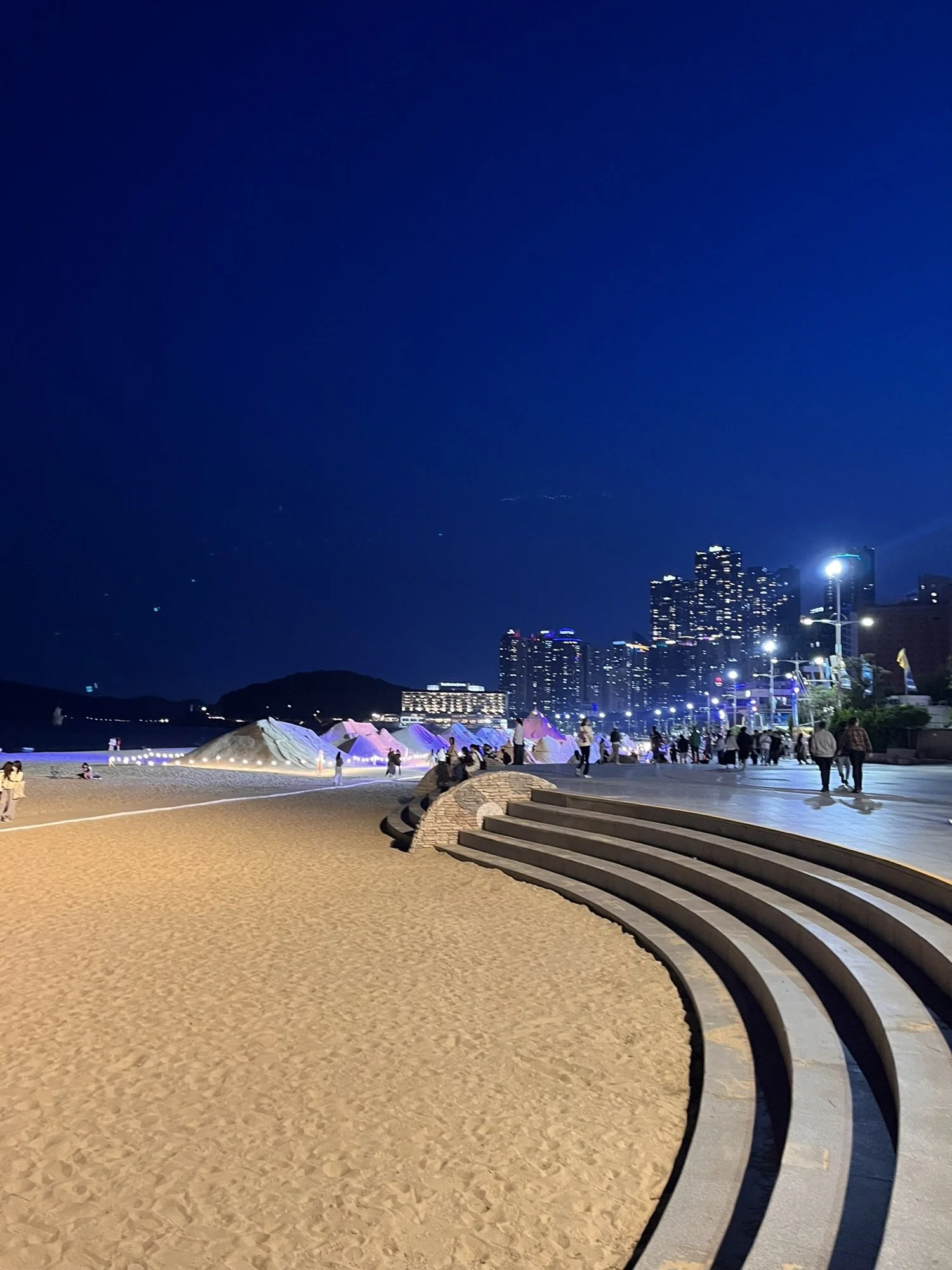 Busan beachfront at night with city lights and people walking on the promenade