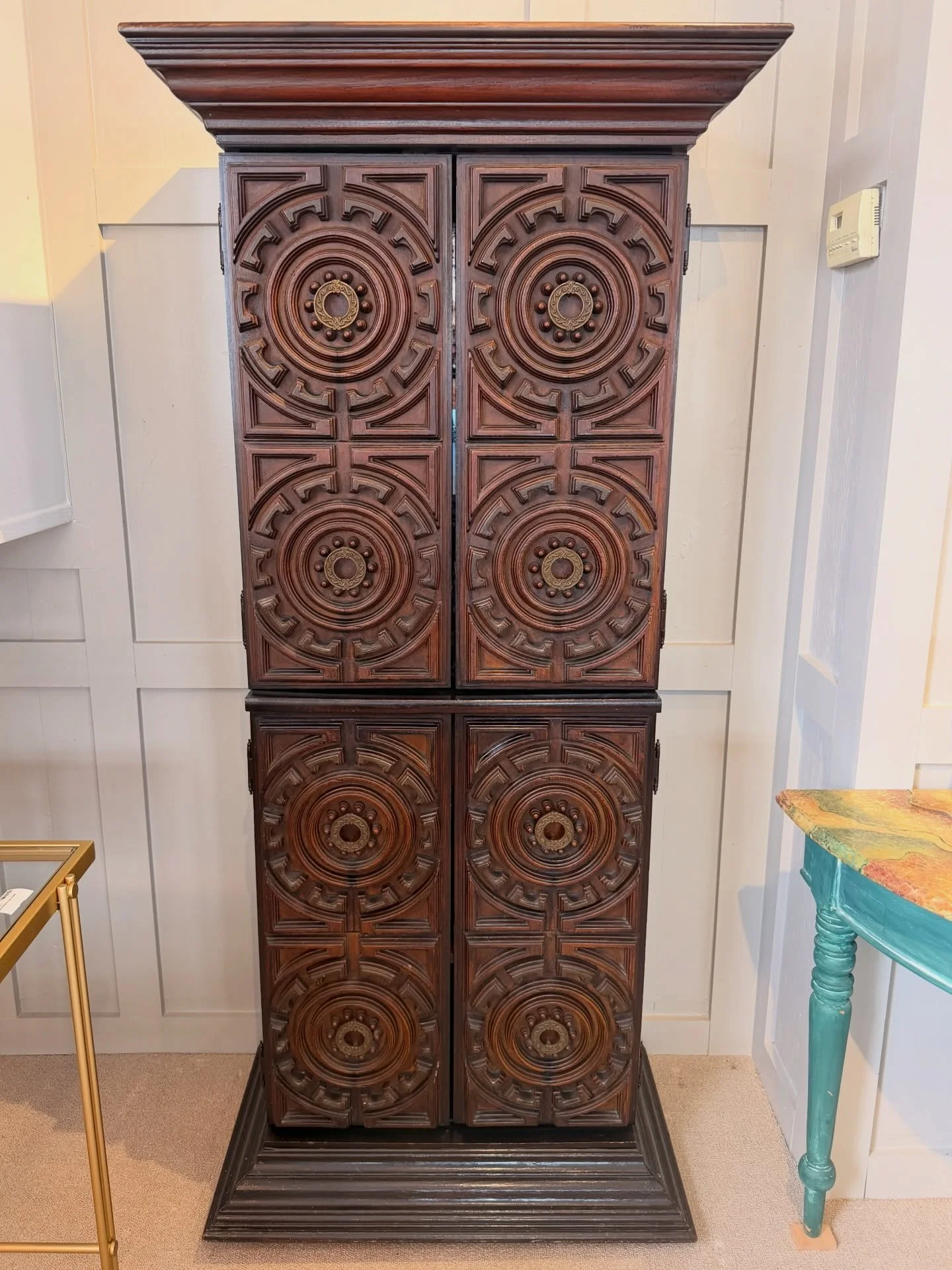 A super cool one of a kind mid-century bar cabinet. This is a great size! Nice and narrow to fit in a small space. Heavily carved with an exaggerated base and crown. The round brass handles open to reveal a smoky glass back. The bottom opens to revea