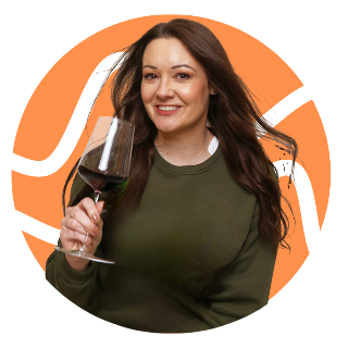 Woman with long brown hair smiling and holding a glass of red wine.