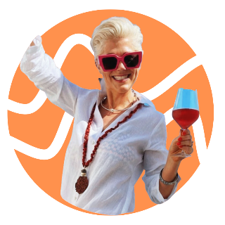 A woman with short blonde hair wearing pink sunglasses, a white shirt, a red beaded necklace, holding a glass of red wine, smiling, against a pink background.