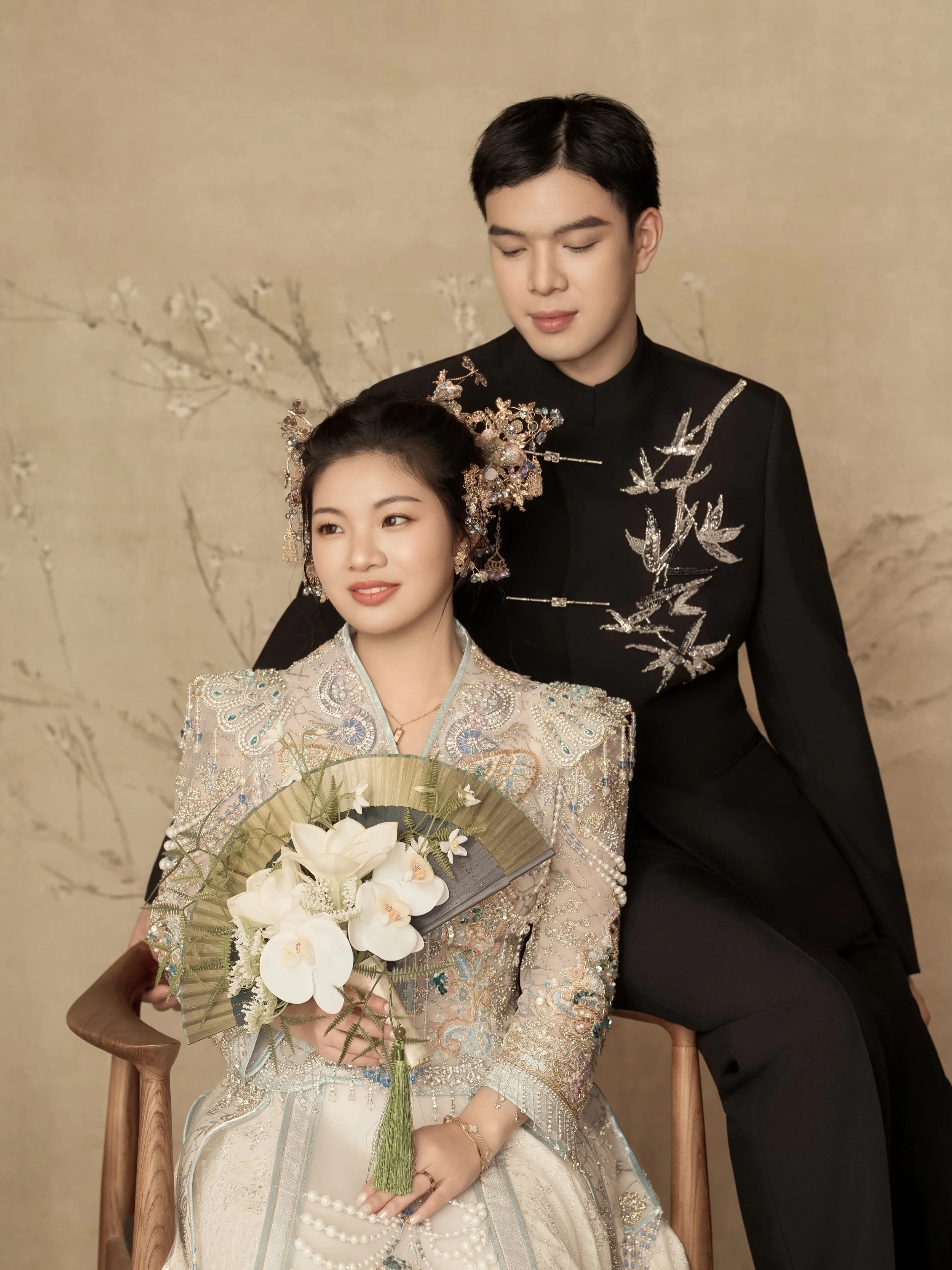 Modern Chinese bridal elegance, softened by studio light. 🤍

There is something quietly powerful about this set. The embroidery feels like a poem stitched into fabric. The floral hairpiece, the ivory bouquet, the warm textured backdrop. Every detail