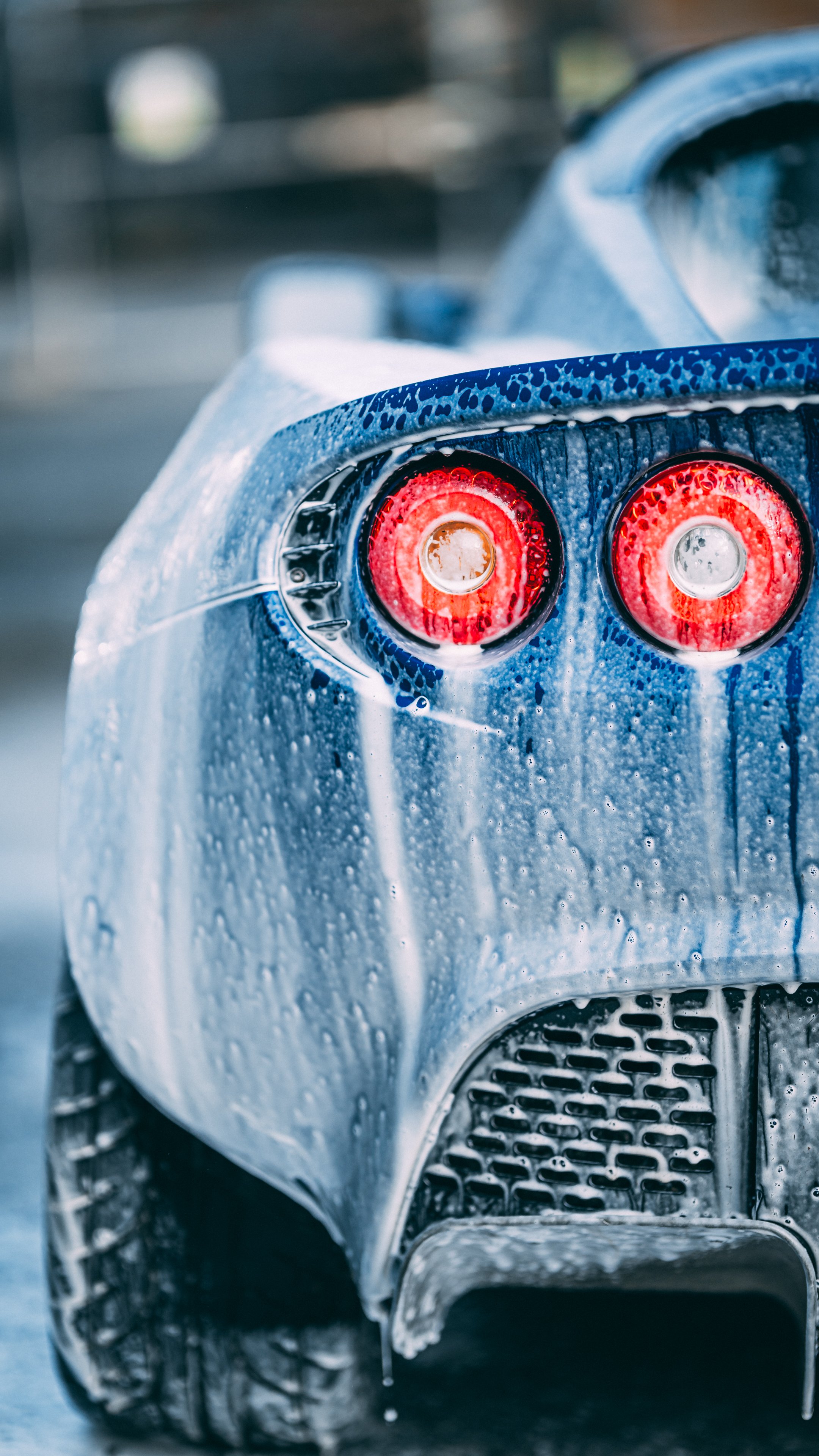 Close-up of the rear of a blue sports car with water droplets and soap bubbles, focusing on the red taillights.