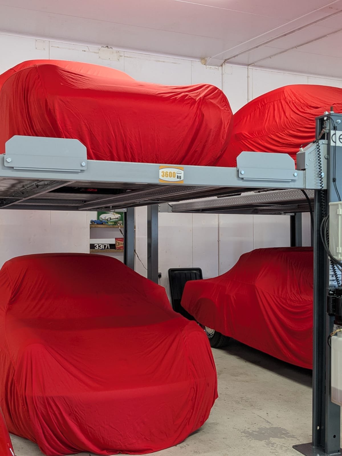 Four cars covered with red cloths stored on a two-level parking rack inside a garage.