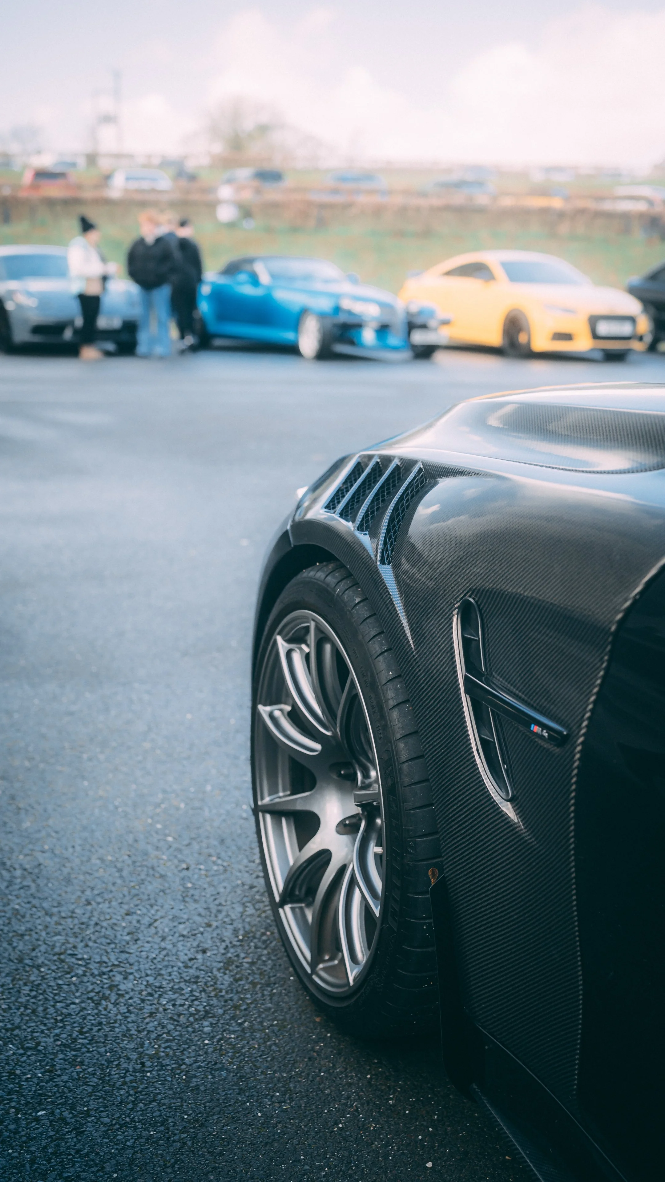 Close-up of the front wheel and fender of a black sports car with carbon fiber details, parked on asphalt.