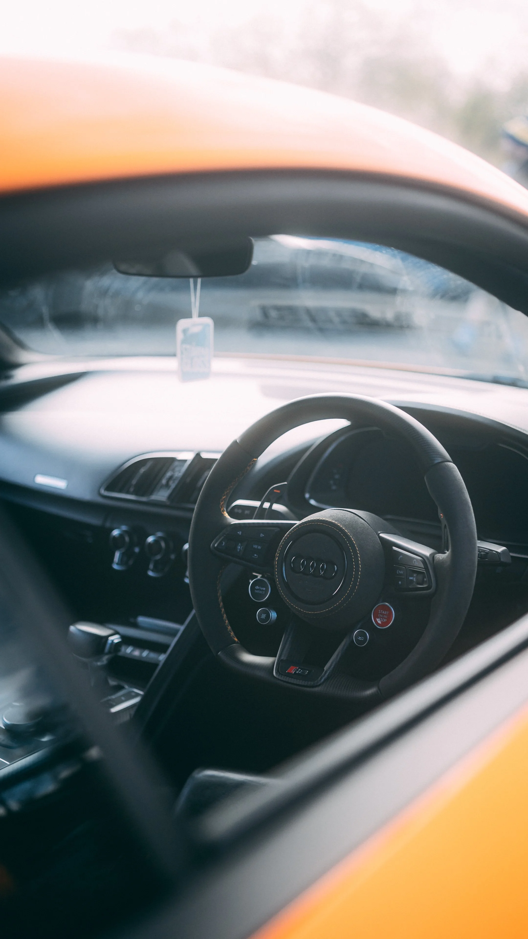 Inside view of a luxury car dashboard and steering wheel, with a yellow exterior visible through the windshield.