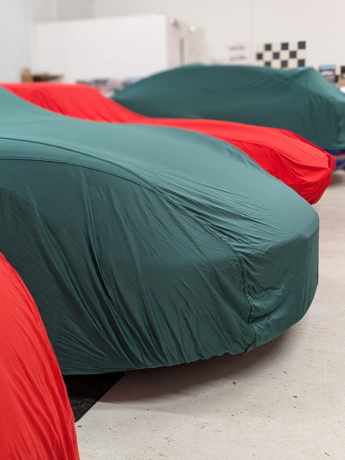 Multiple cars covered with teal and red car covers in a showroom or garage.