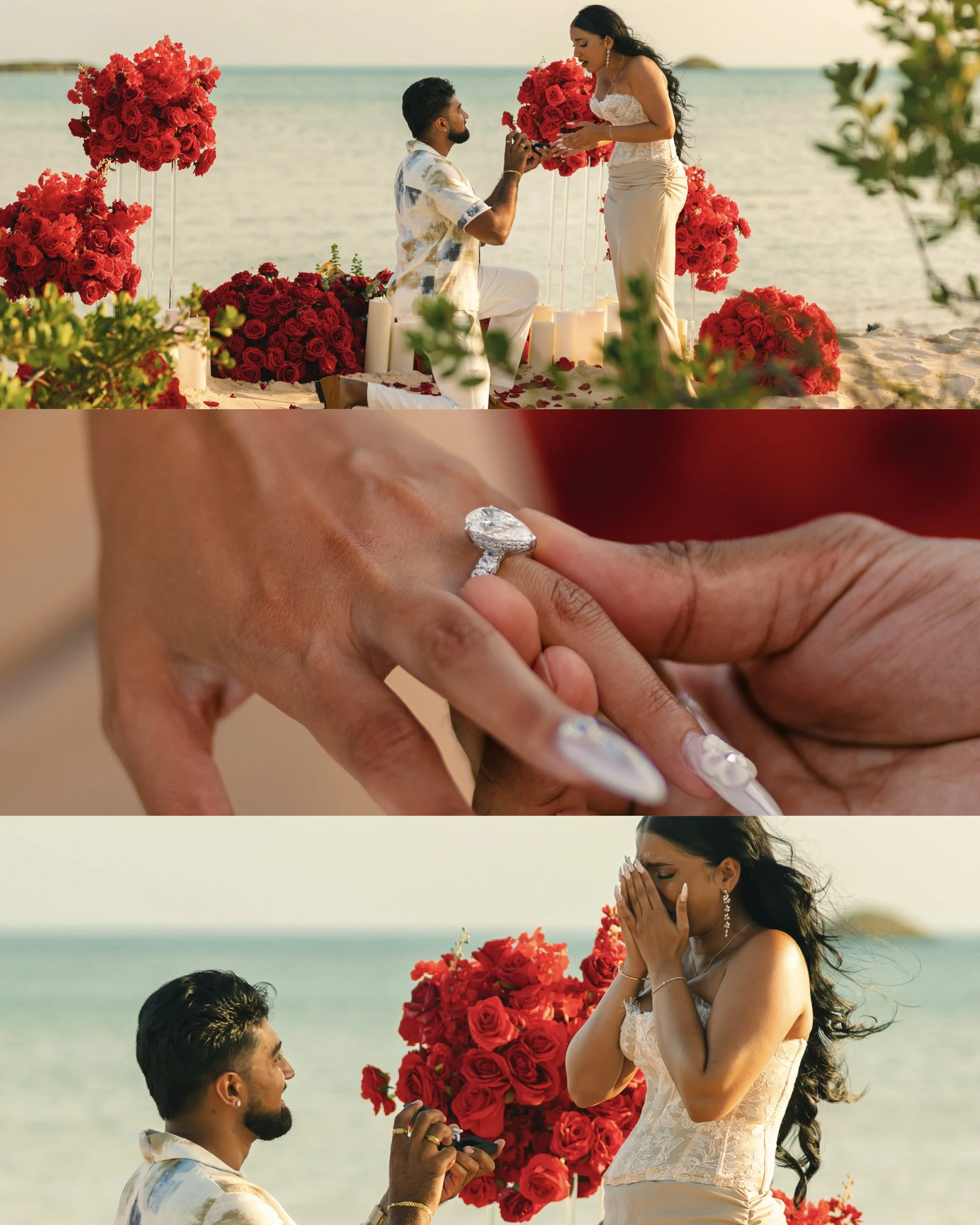 A couple is having a marriage proposal on a beach, with the man kneeling and holding a ring, and the woman covering her face with her hands, surrounded by red roses and candles, against the ocean backdrop.