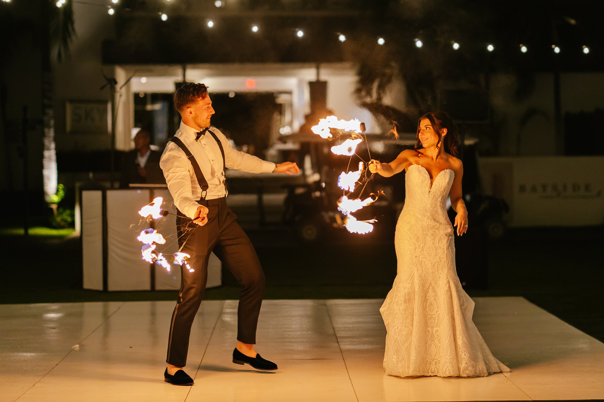 A bride and groom performing fire dance at night, with string lights overhead.