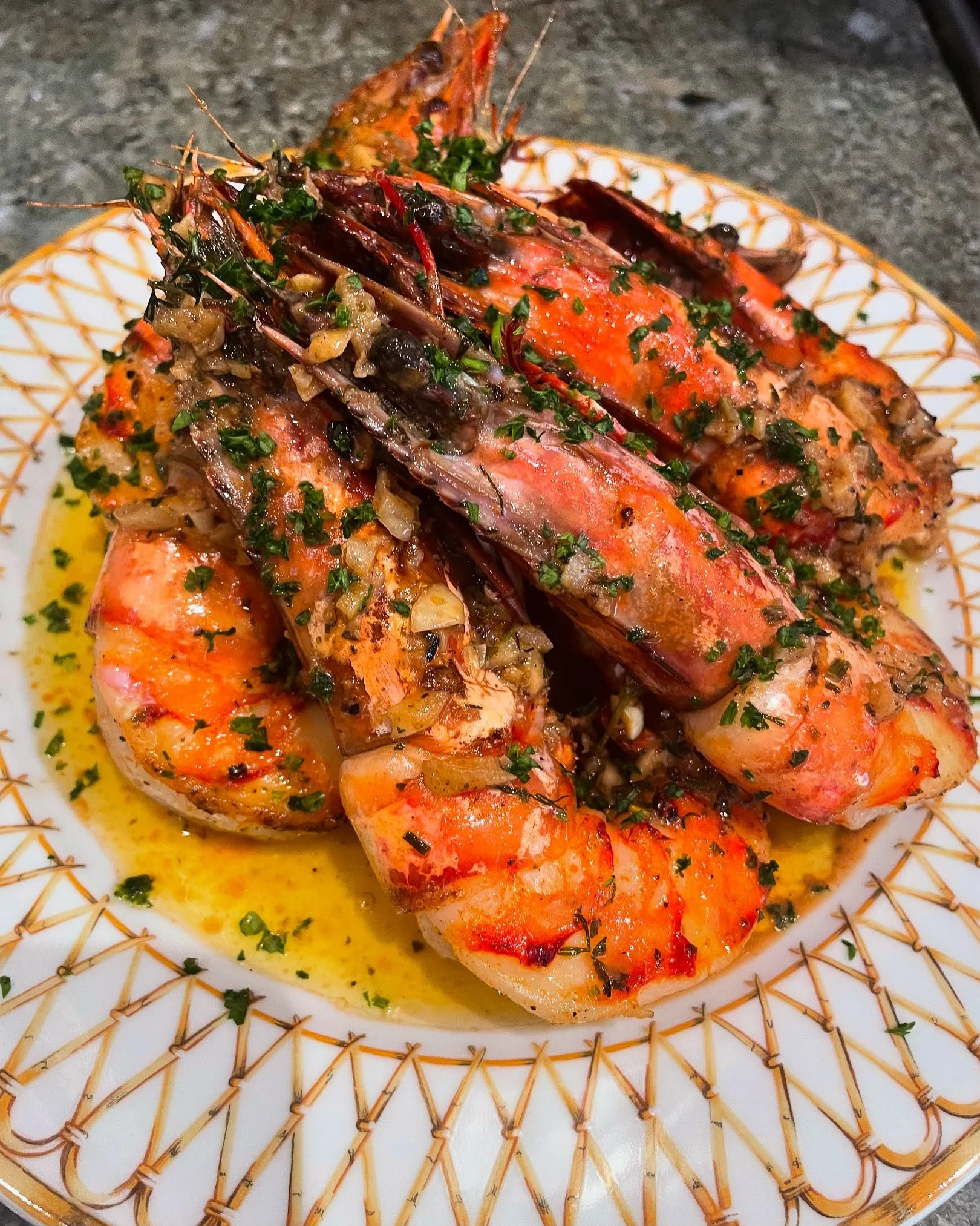 Close-up of grilled lobster tail topped with herbs and seasoning, served on a patterned white plate with a yellow sauce.