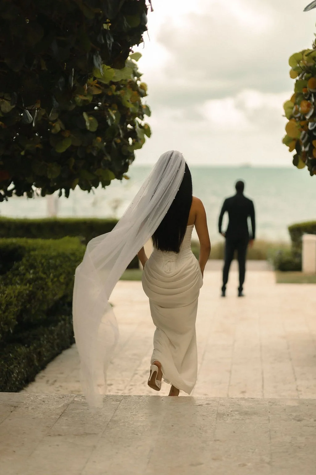 Natasha walking toward Jacob with her veil flowing along the resort path.