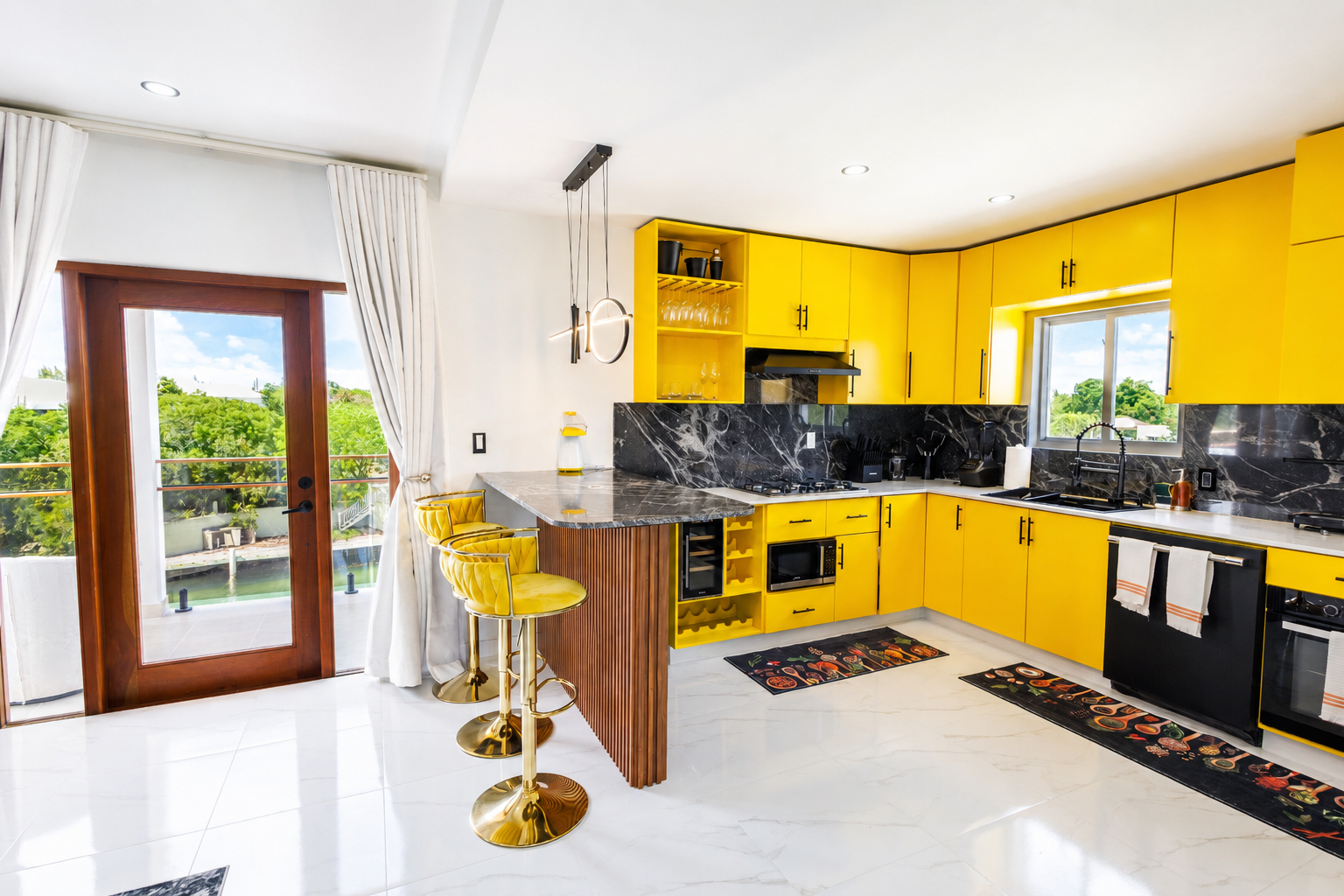 Bright yellow kitchen with black marble countertops, white flooring, and outdoor view through windows and sliding door with curtains.