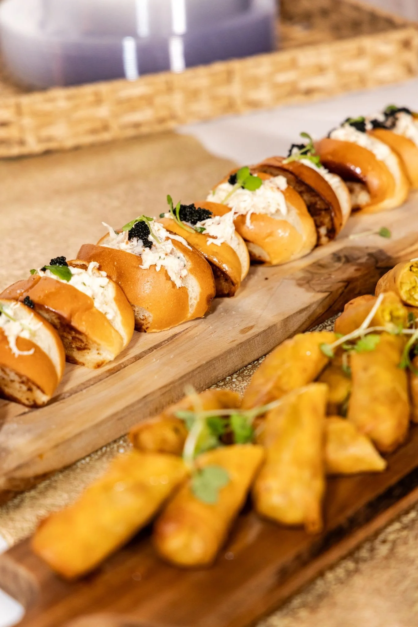 Close-up of a row of sandwiches with various fillings, garnished with microgreens, served on a wooden board.