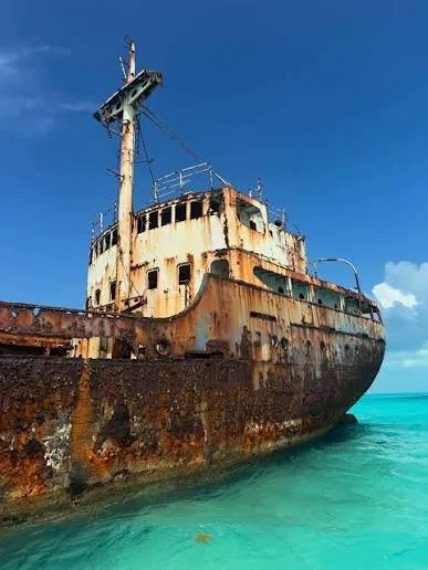 An old, rusted shipwreck partially submerged in turquoise water under a blue sky.