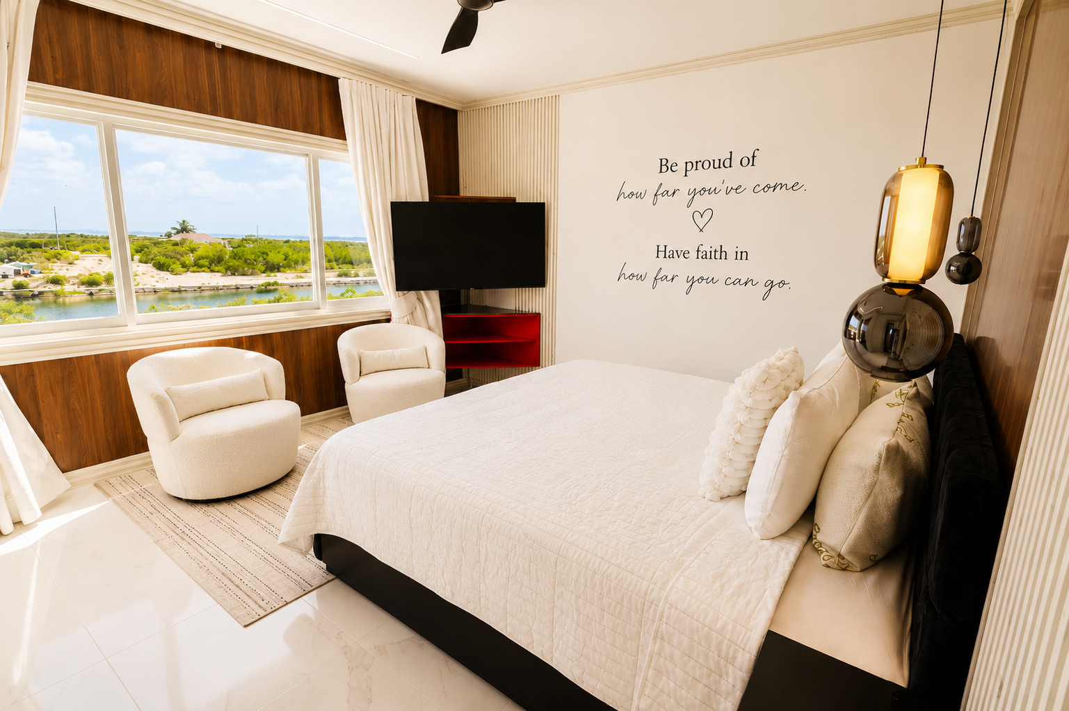 Bright bedroom with large windows, white bed with multiple pillows, wall decor with inspirational quote, two white armchairs, television, and modern lamp