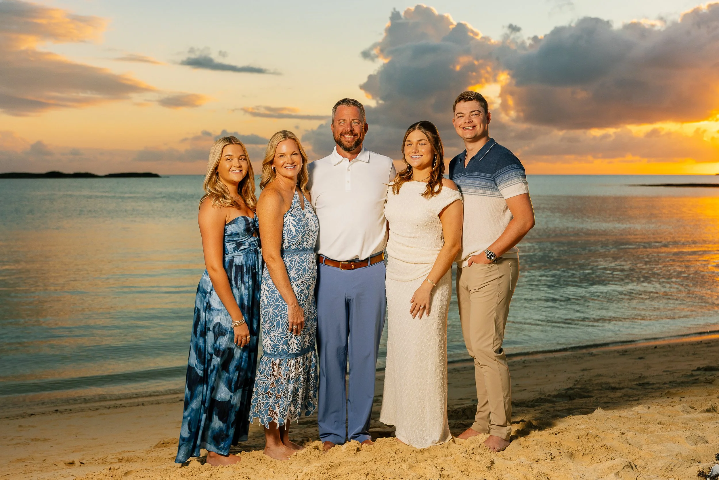 Turks and Caicos photographer with a Group of five people standing on a beach at sunset, smiling, with water and clouds in the background, dressed in summer clothing.