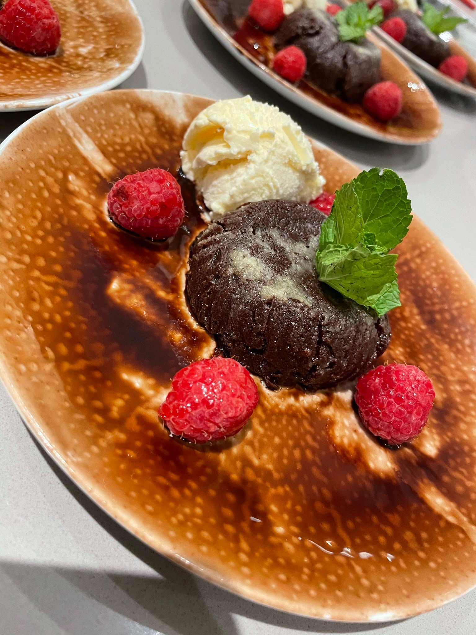Dessert bowl with ice cream, raspberries, a mint leaf, chocolate cake, and berry sauce.
