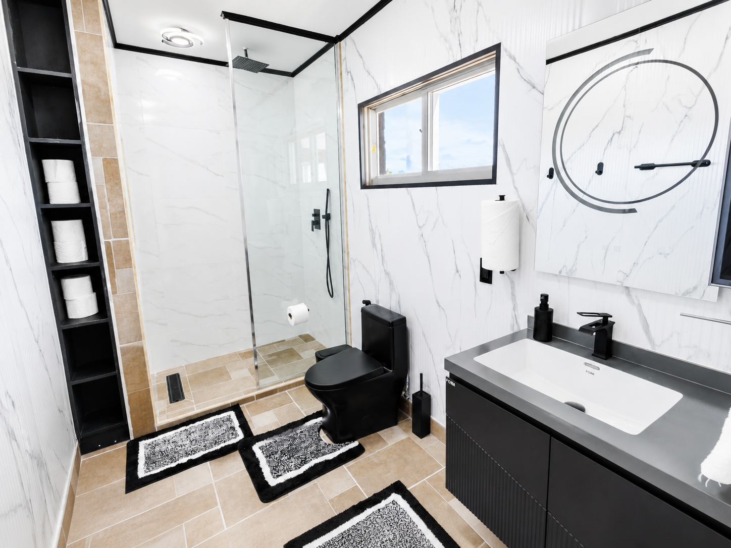 Modern bathroom with a walk-in shower, black toilet, black vanity with a white sink, and a window with blue sky view. Black and white rugs on tan tile floor.