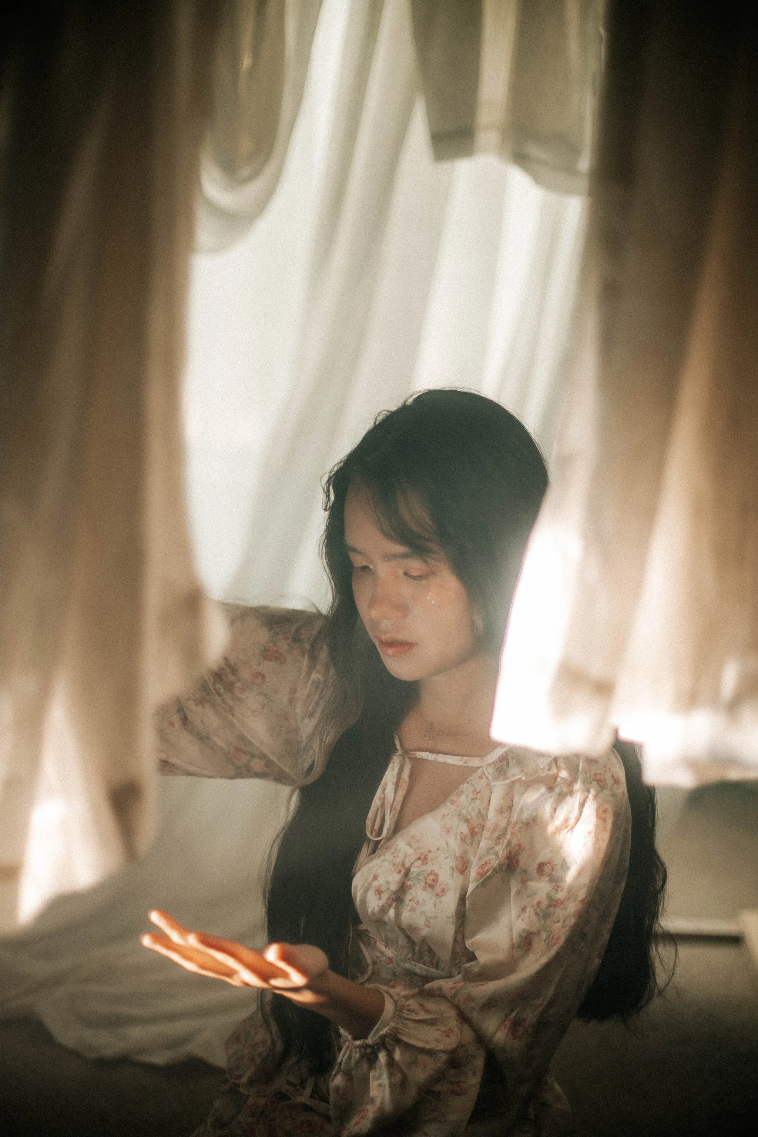 Decorative scene with two lit candlesticks, a mirror with a gold frame, a white vase shaped like a head filled with yellow flowers, and a small shell dish on a marble surface.