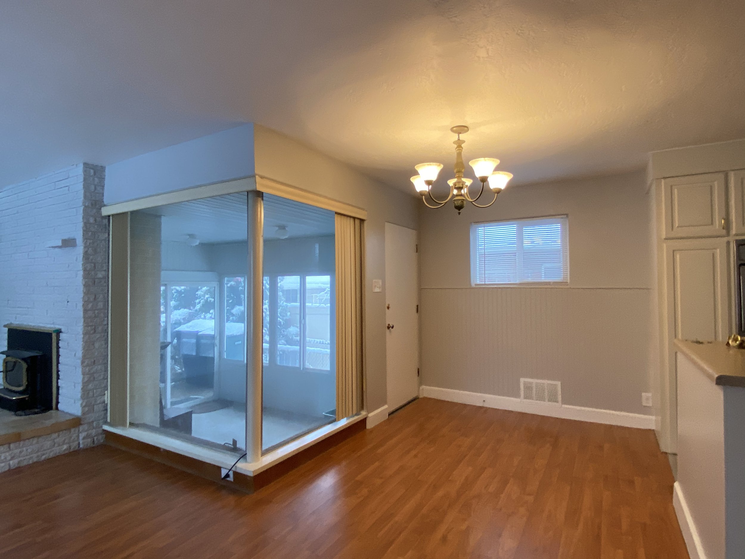Living room with hardwood floors, a chandelier ceiling light, and large windows. There is a screened porch visible through sliding glass doors.
