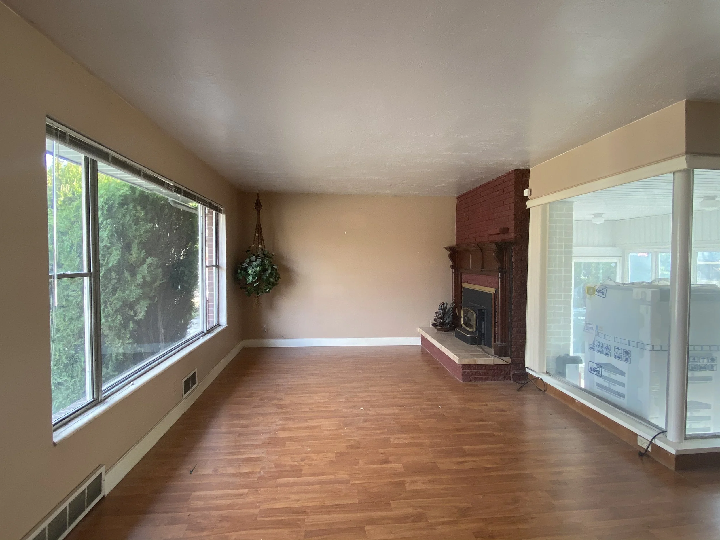 Empty living room with large windows, a fireplace, a potted plant, hardwood floors, and a sliding glass door leading to an outdoor space.