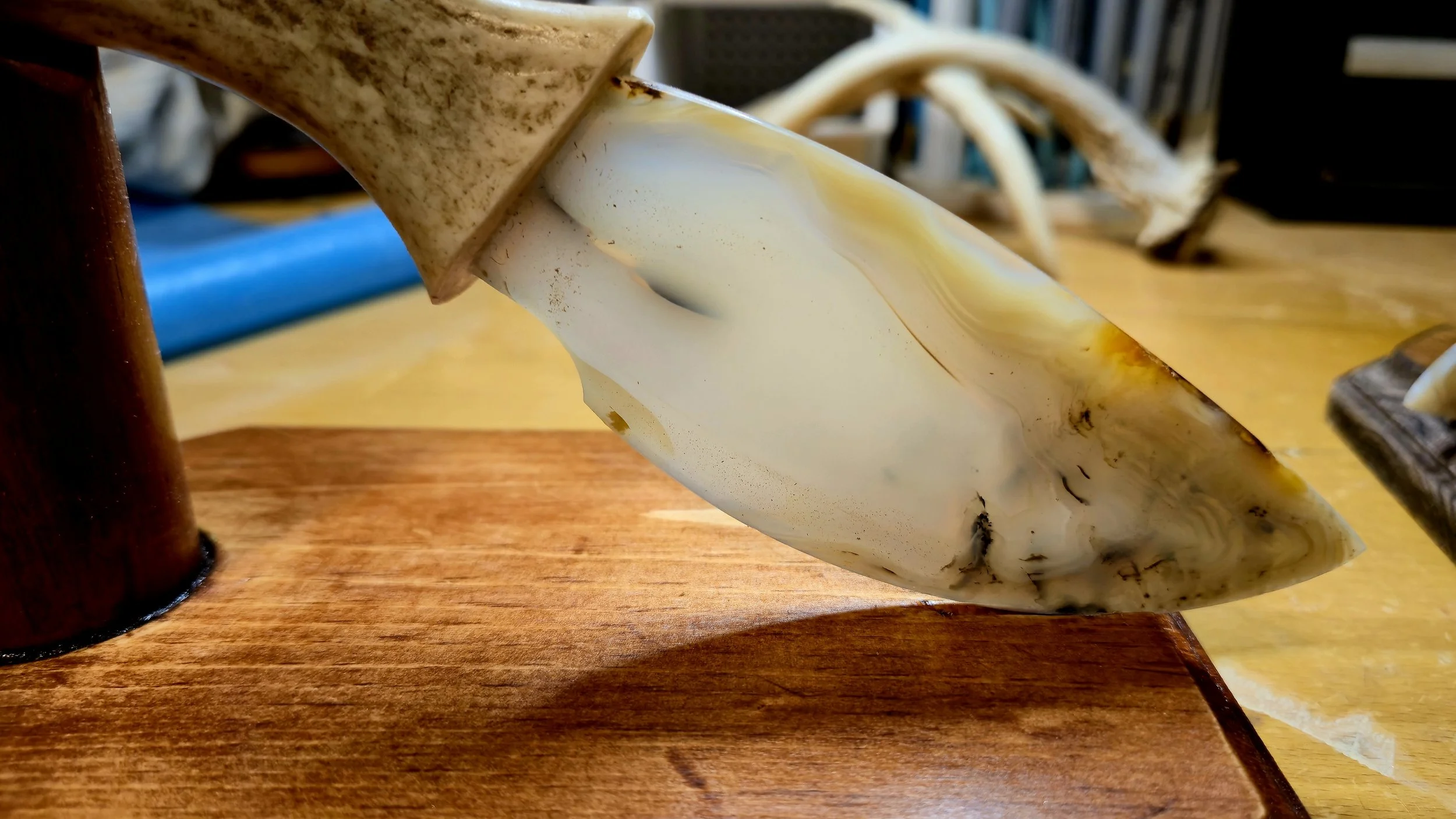 Close-up of a large, stylized knife or blade with a marbled cream and brown handle, resting on a wooden surface.