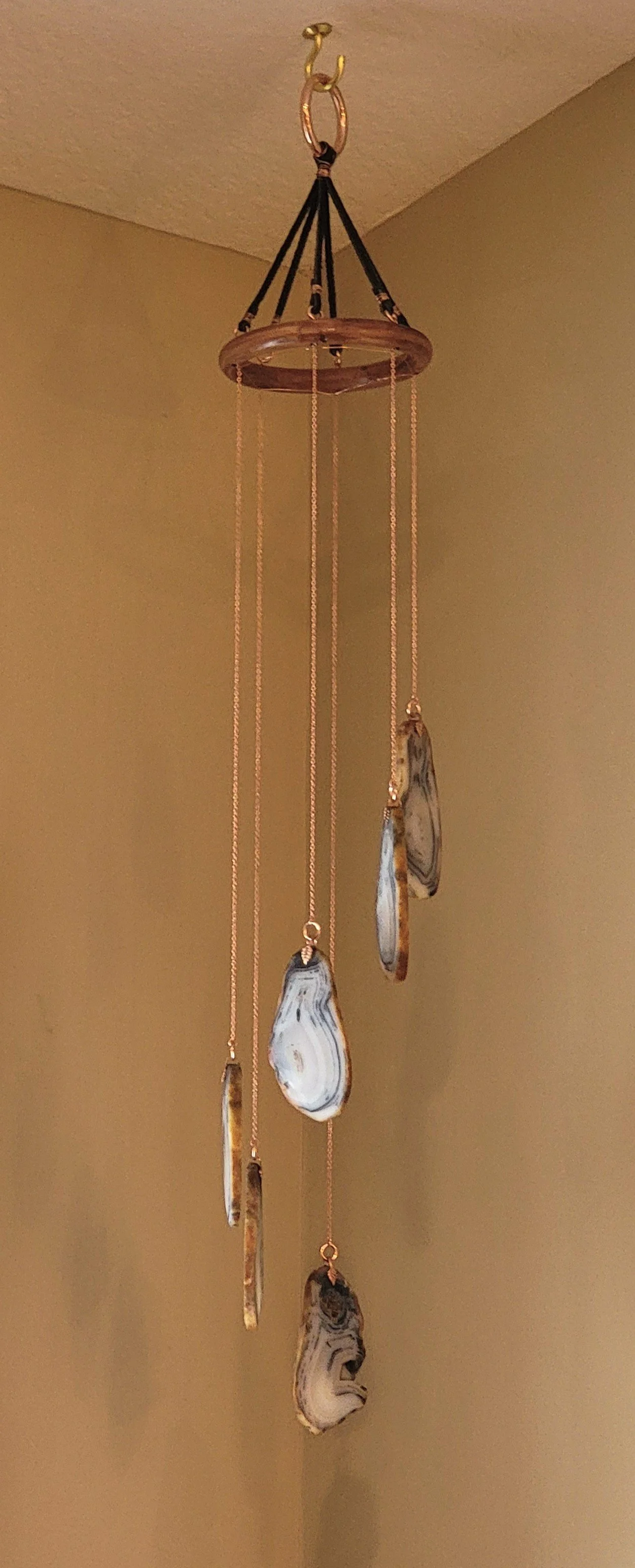 A decorative wind chime hanging from a ceiling hook, with multiple elongated and oval-shaped stones attached to thin chains.