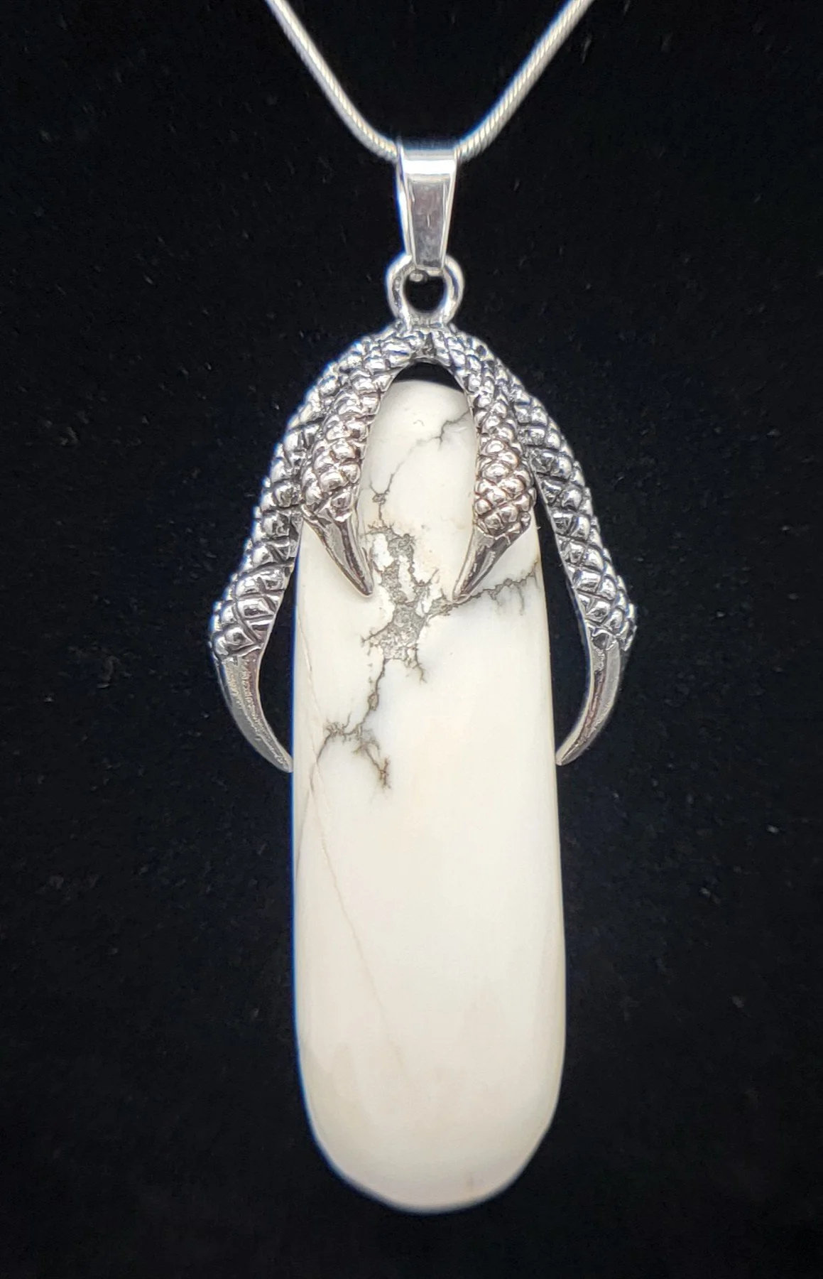 A silver necklace with a pendant featuring a large Halite stone with gray veining, shaped like an egg in a claw or talon.
