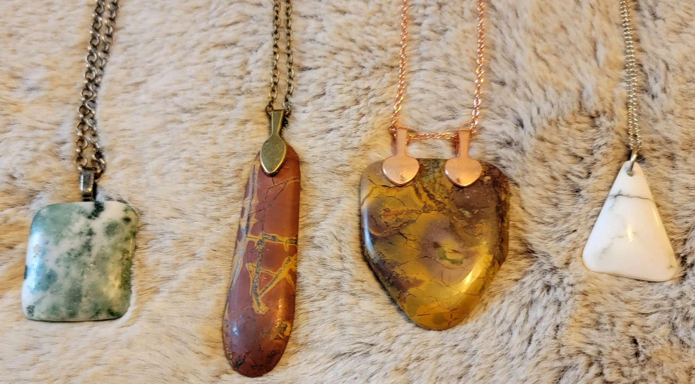 Four necklaces with large stone pendants on a beige furry surface