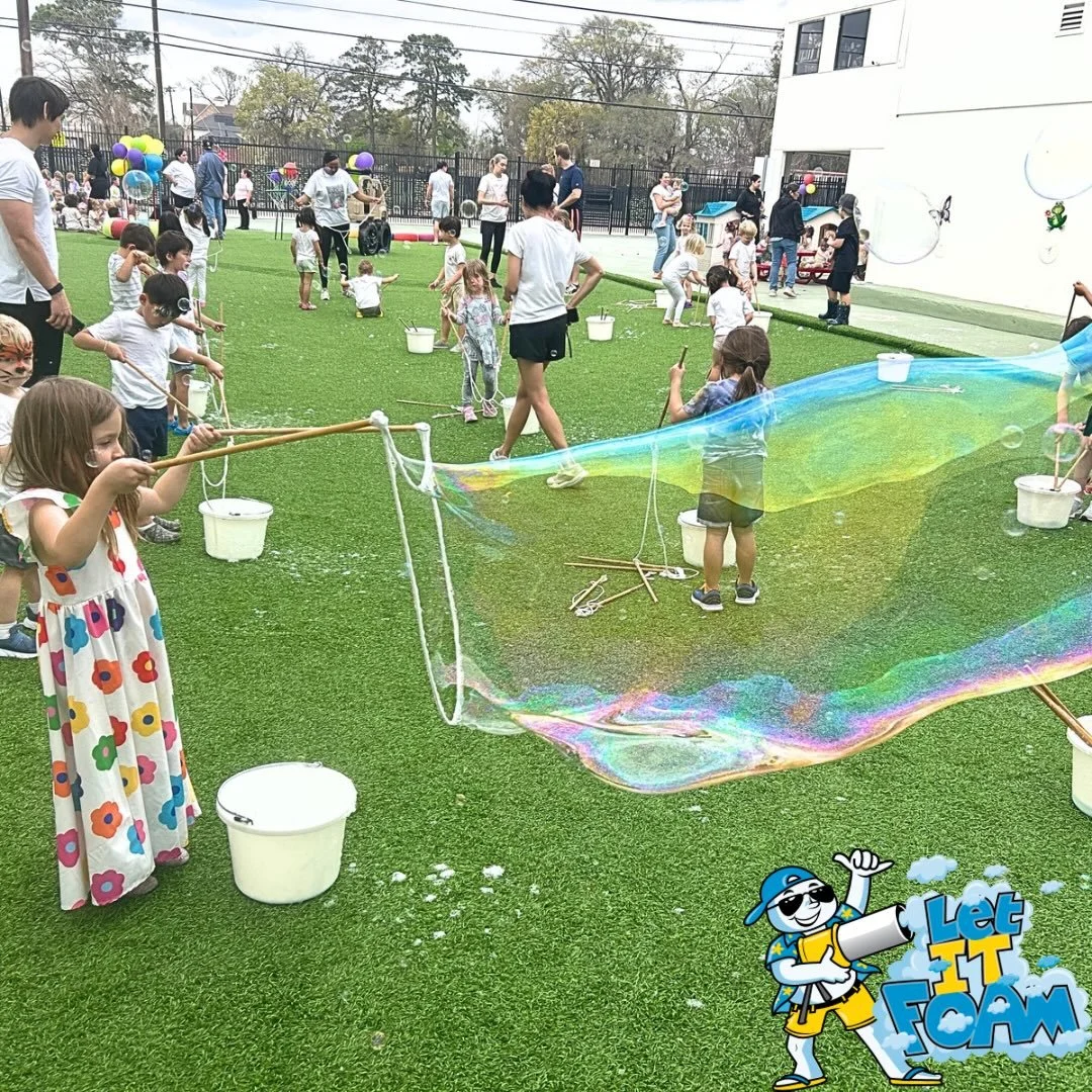 Two children playing with bubbles created by a bubble maker in a backyard with a wooden fence and trees in the background.