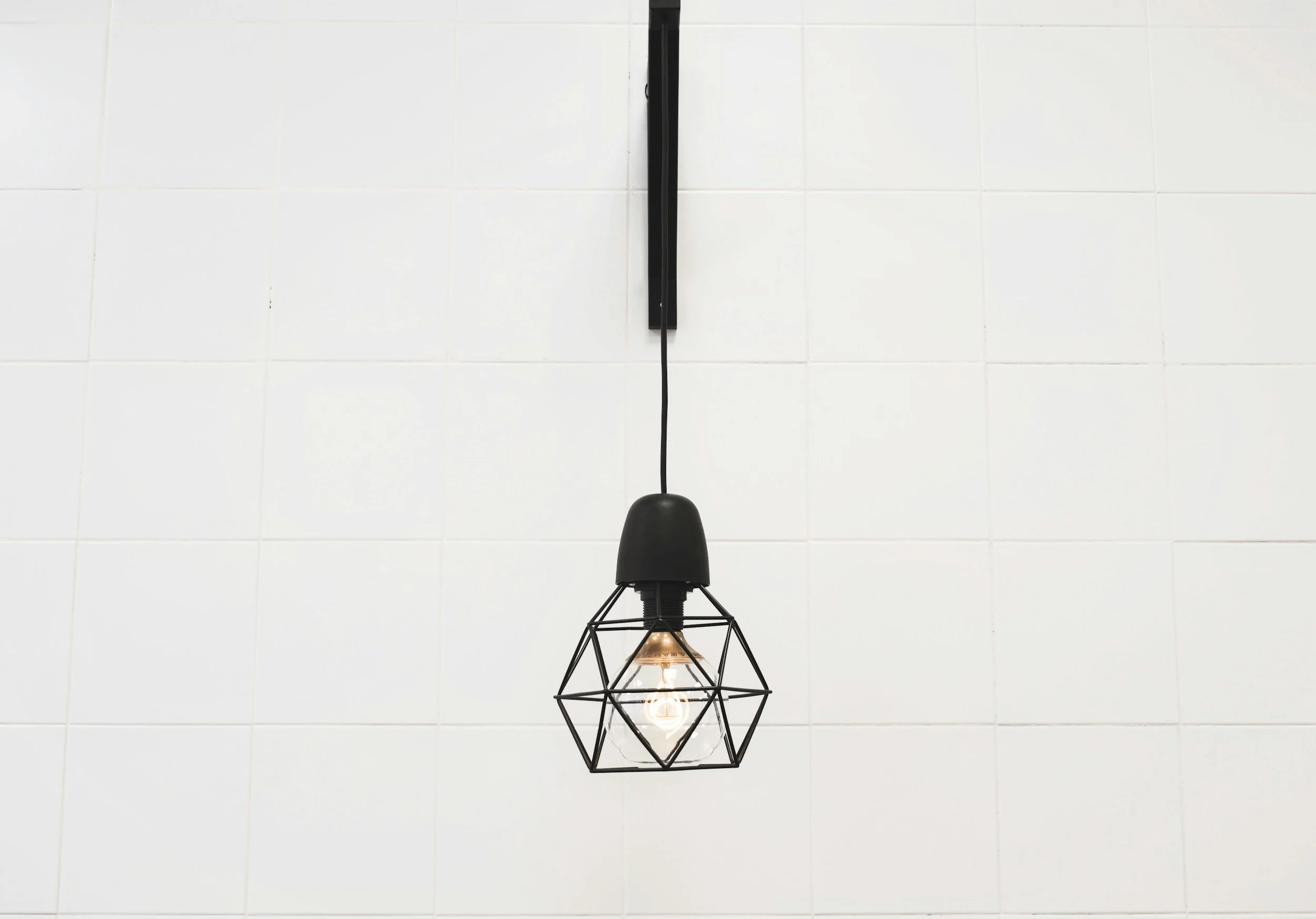 Black industrial lamp with an edison bubble on a white tiles background. A simple and minimalist image to represent Clarity, Simplicity, and Minimalism.