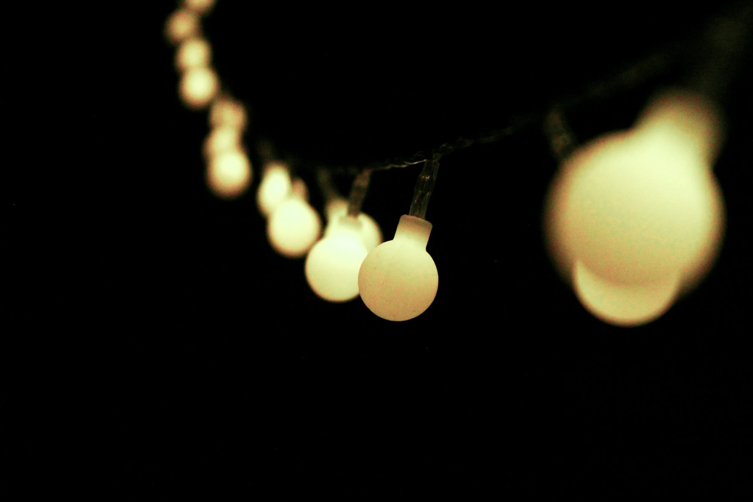 A line of light bulbs hanging from a cord, that crosses a dark space