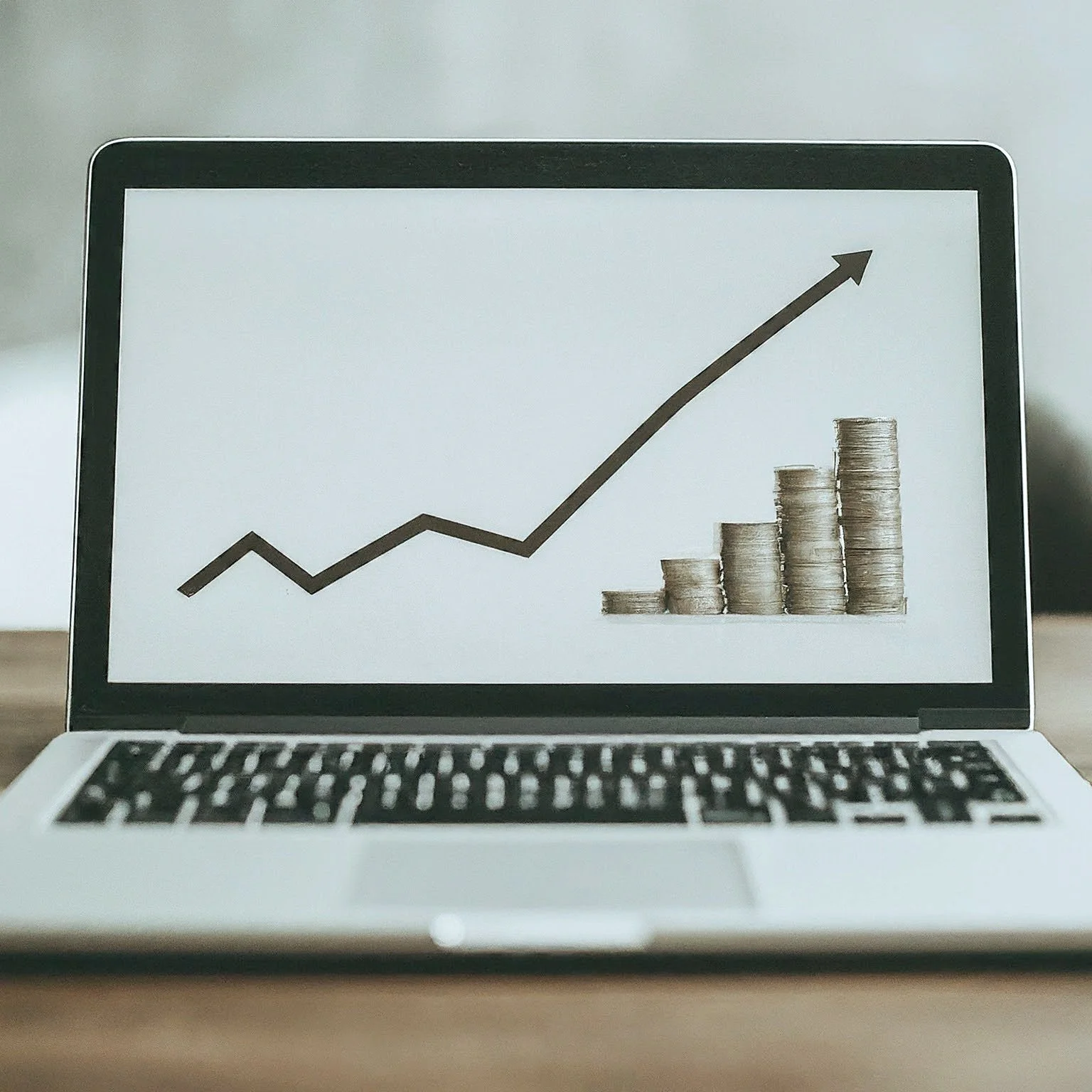 Laptop image with 5 piles of coins on the right bottom corner of the screen, and a trend arrow starting in the left bottom corner that goes up to the right top corner after some fluctuations