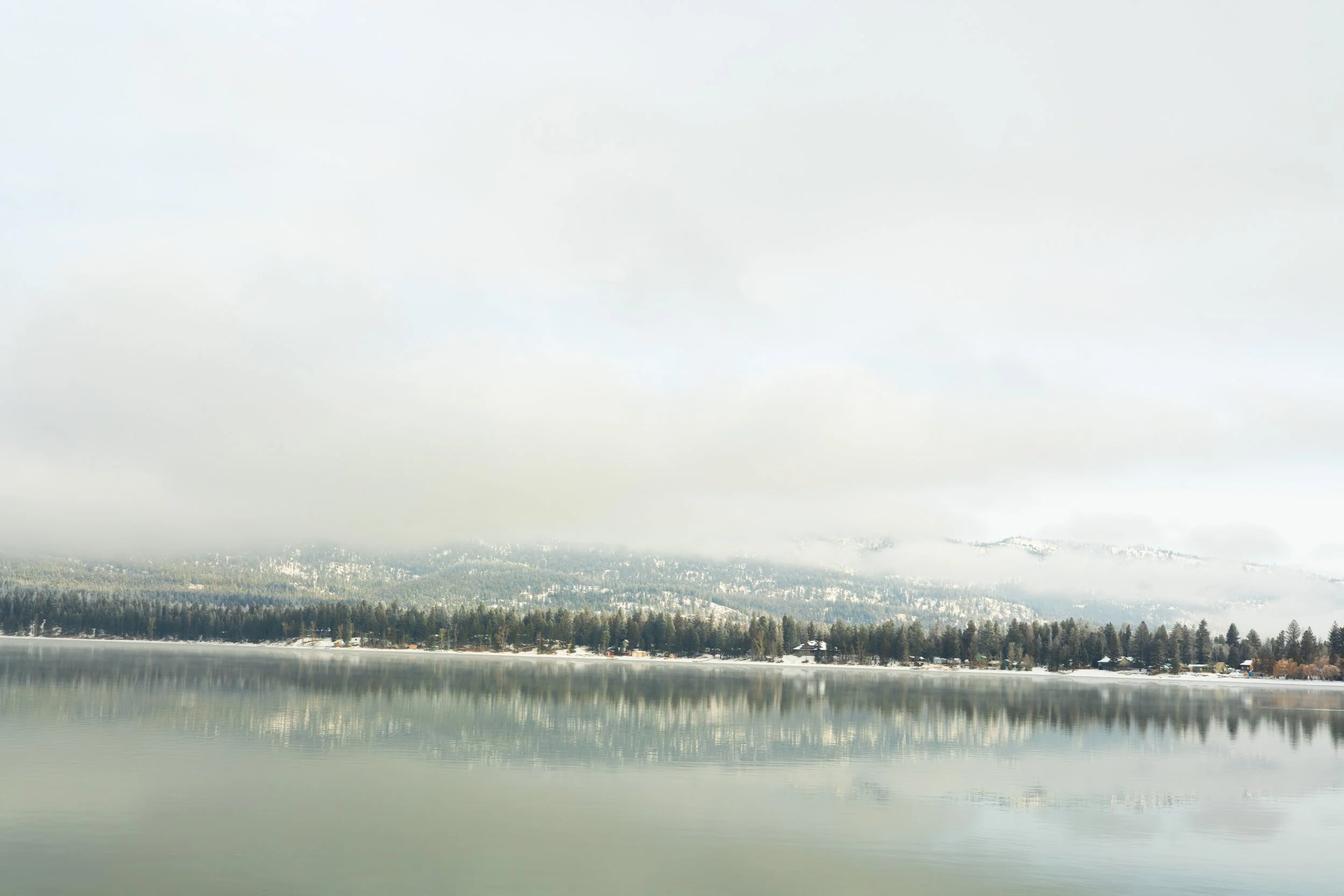 Calm lake with foggy mountains and forest in the background