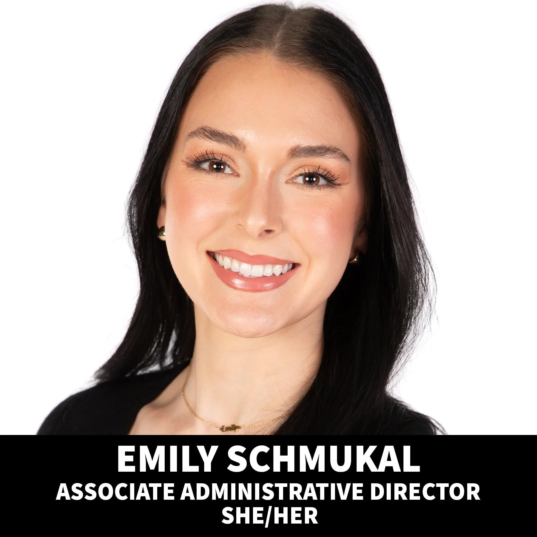 A professional headshot of Emily Schmukal, a woman with long dark hair, smiling, wearing a black sleeveless top, and accessorized with small earrings. The background is plain white, and the lower part of the image has text with her name, role, and pronouns.