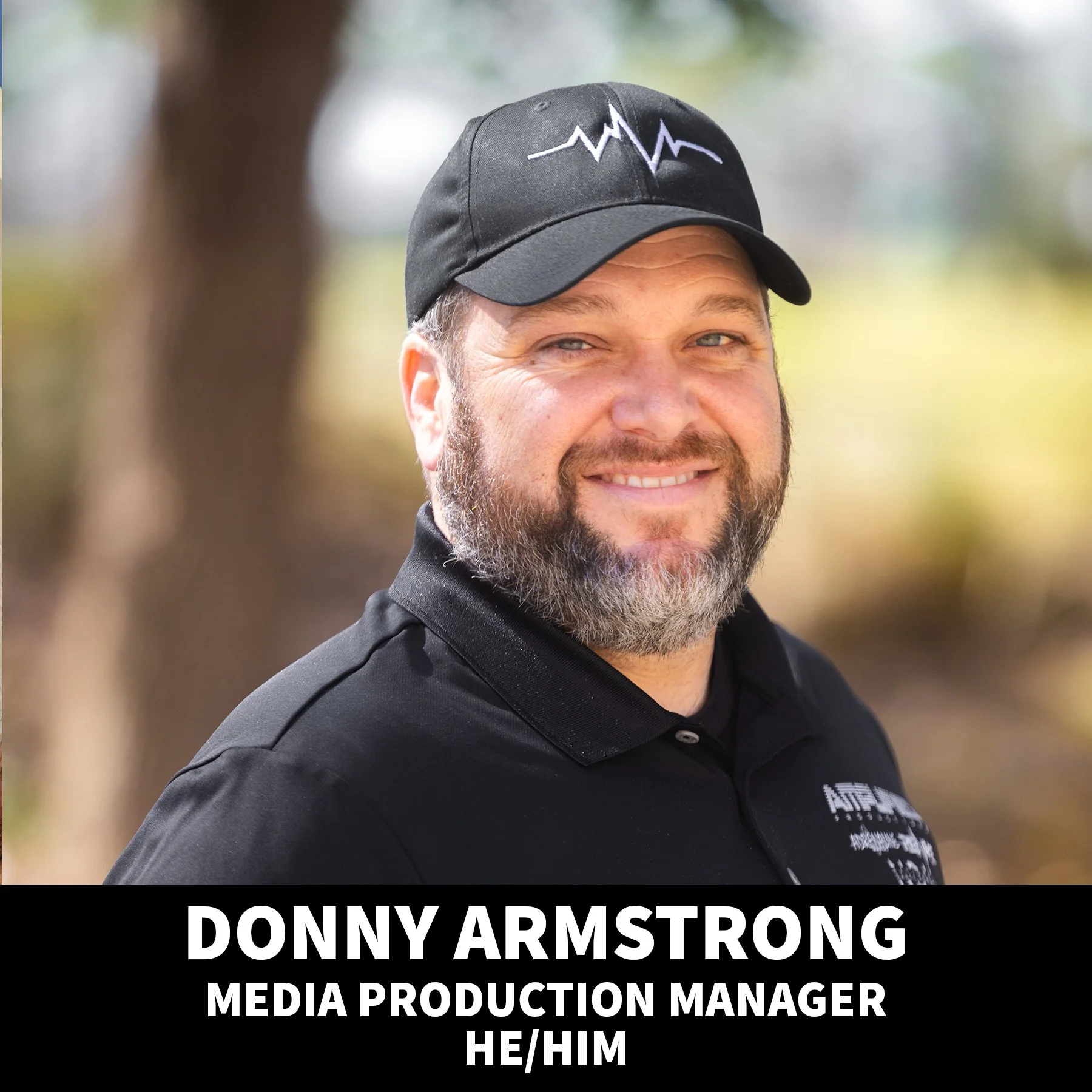 Close-up portrait of Donny Armstrong, a man with light skin, blue eyes, and a brown beard, smiling at the camera, wearing a red shirt, with a white background.
