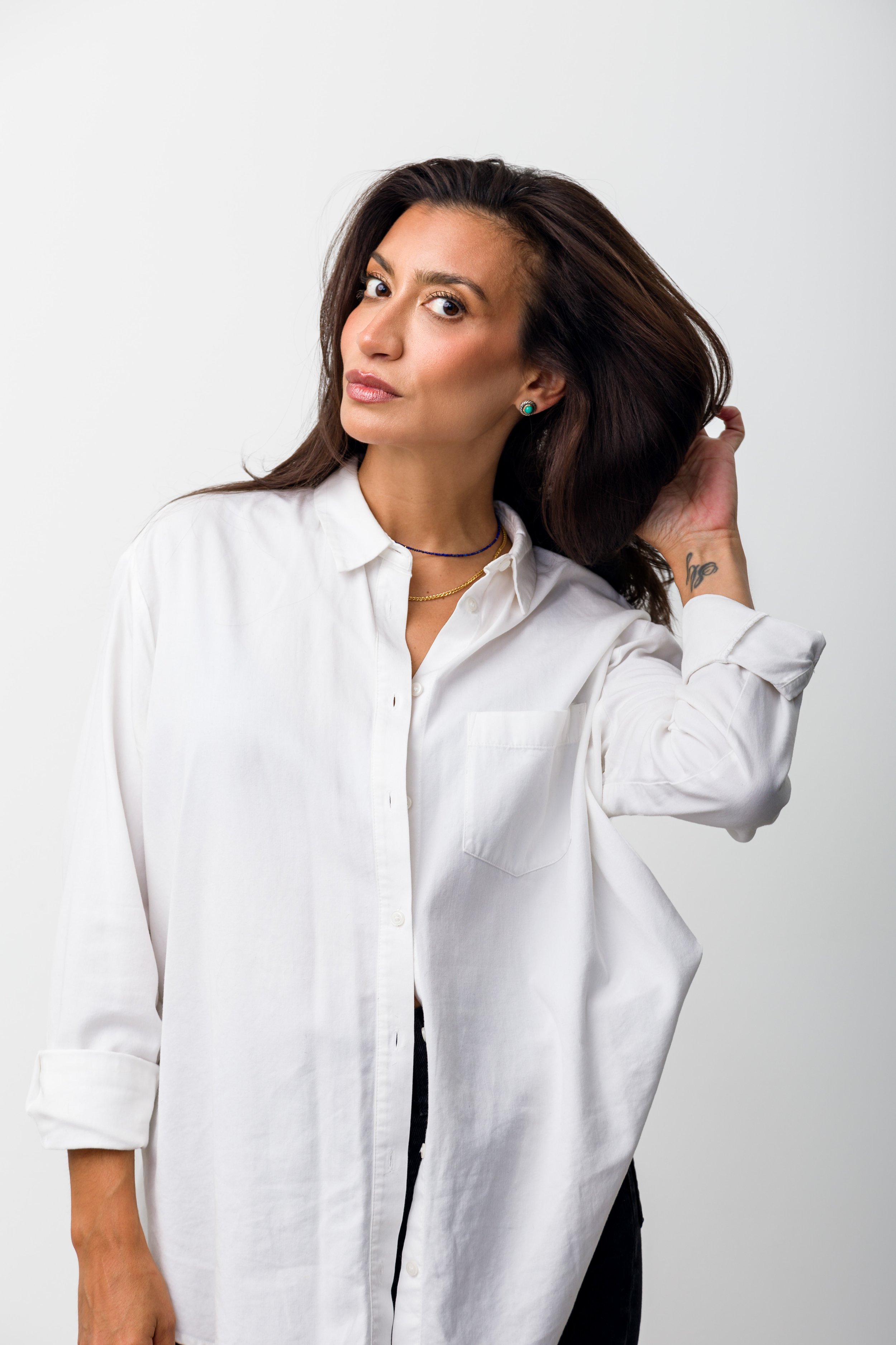 Person in a white shirt with brown hair holding it back and a tattoo on the wrist.