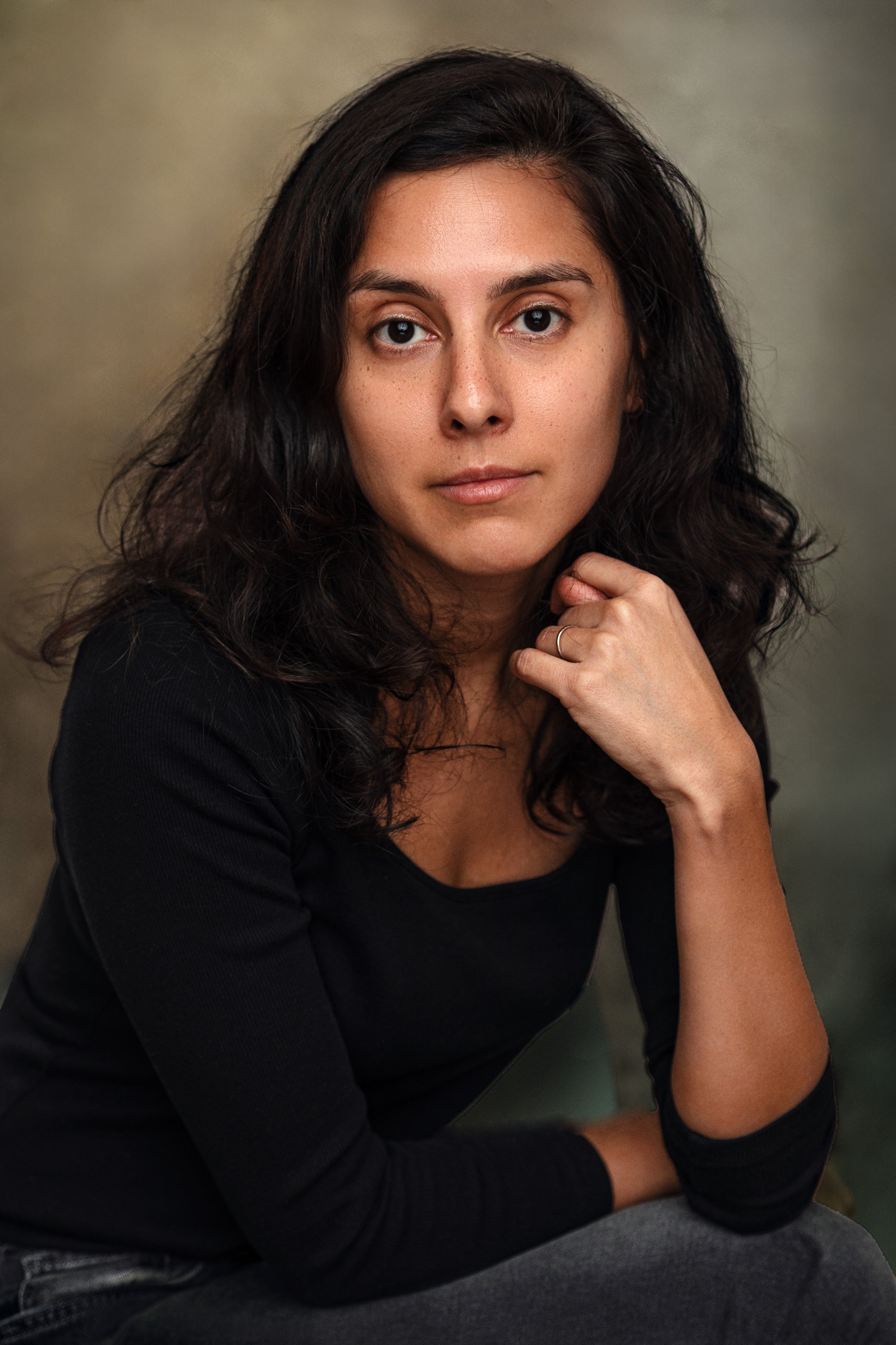 Portrait of a woman with long dark hair, wearing a black top, looking at the camera with a neutral expression.