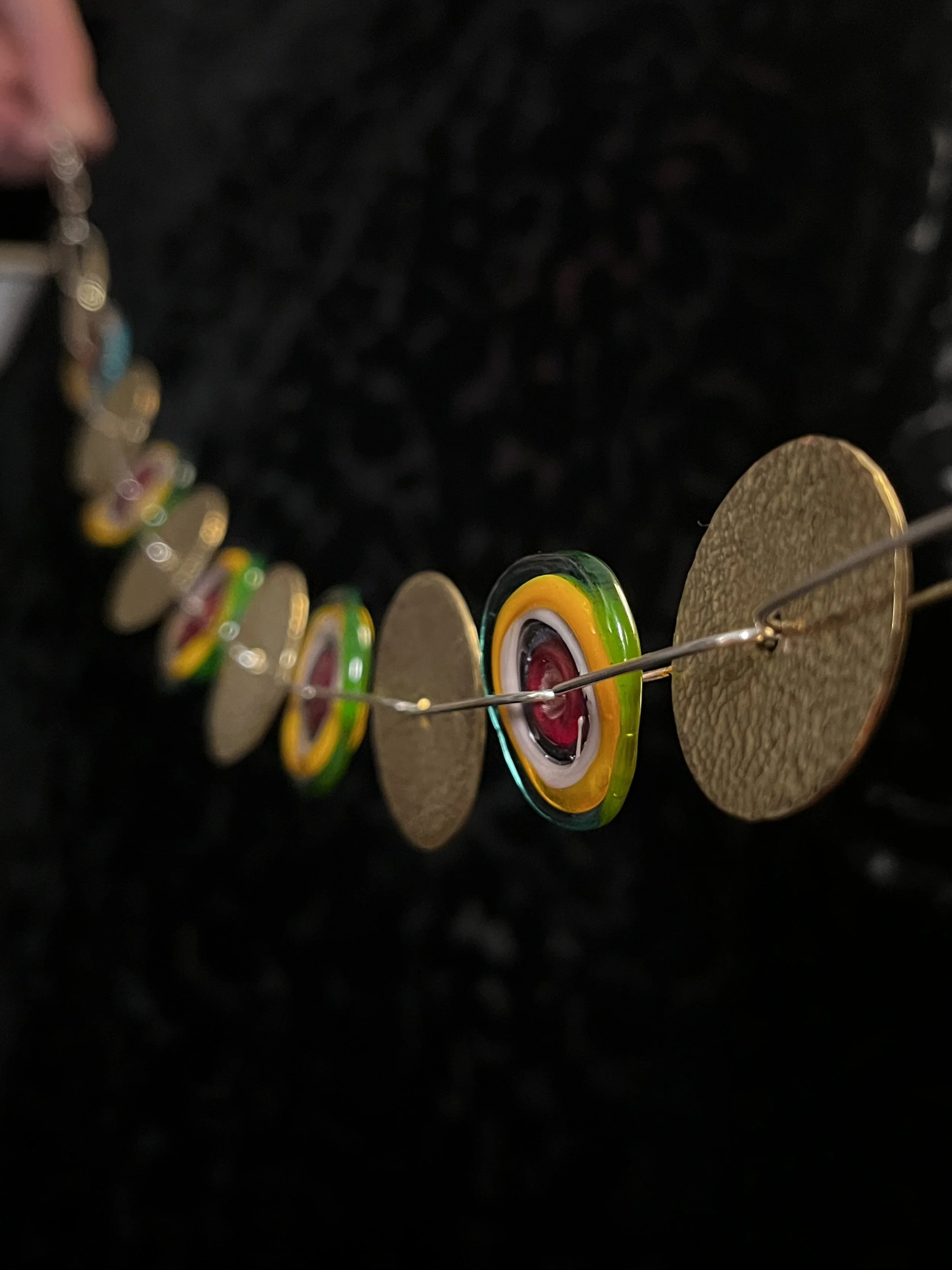 Close up of a necklace made of alternating discs of textured brass and colored glass, connected by silver links.