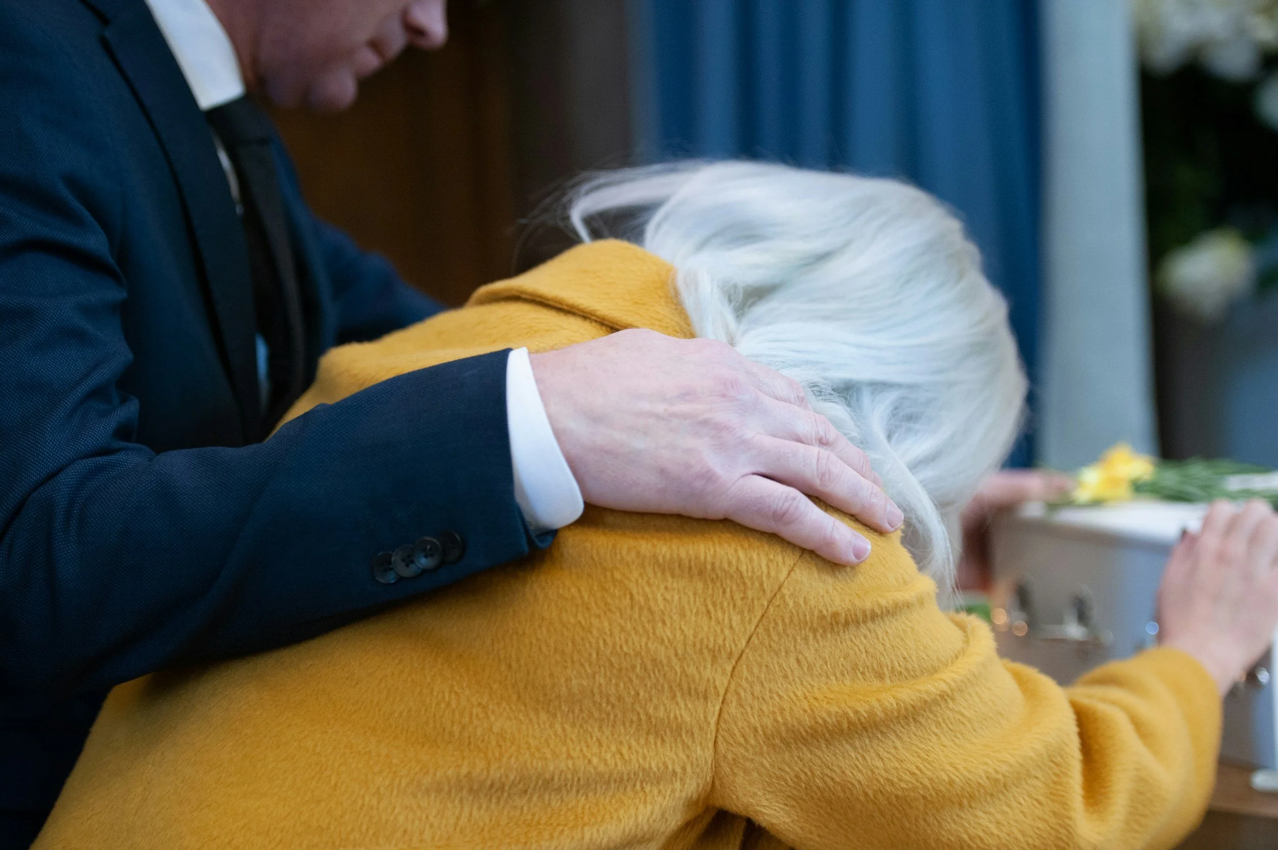 woman wearing a yellow coat at a funeral who is emotional from grief and loss