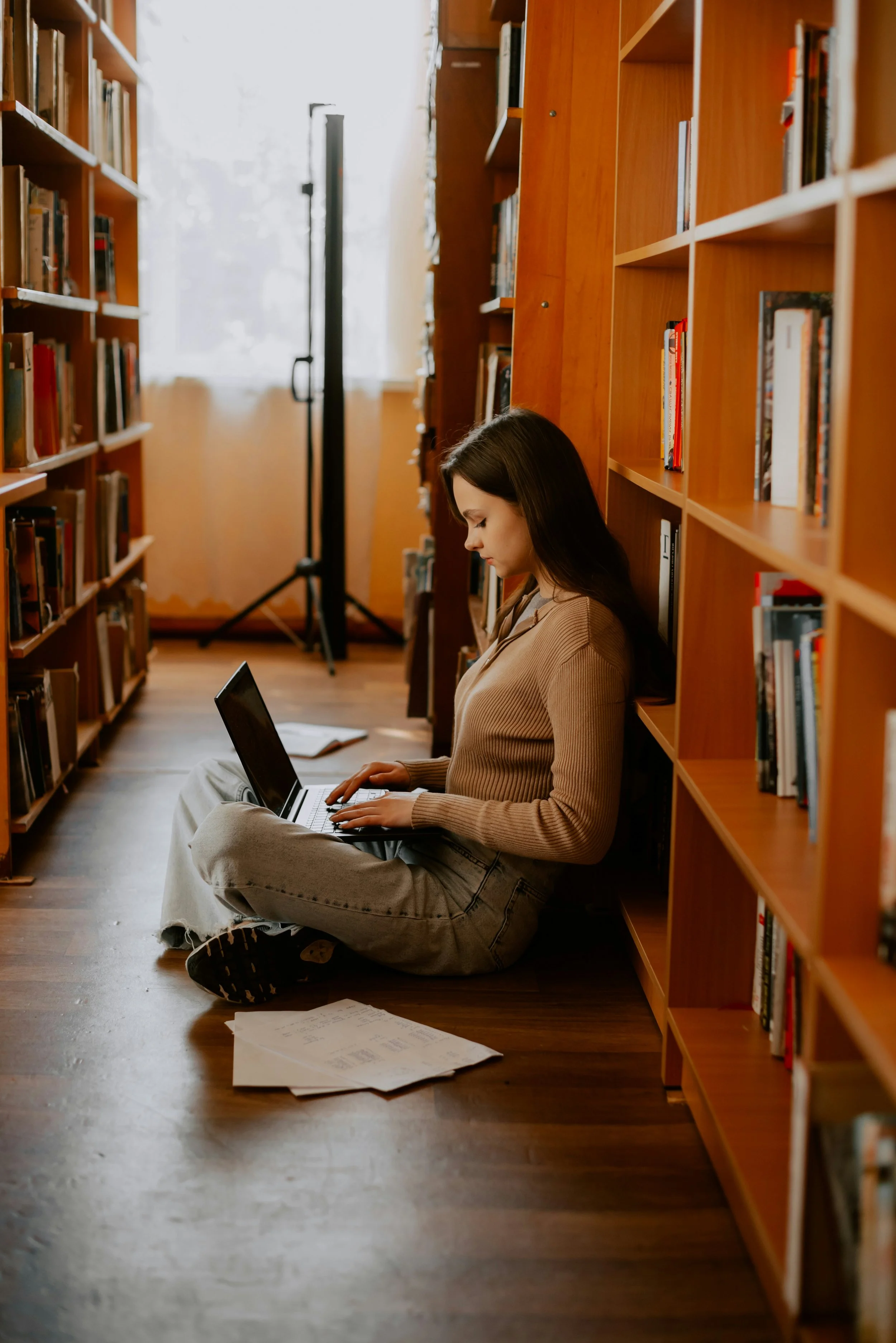 A woman sitting in a library typing in a laptop