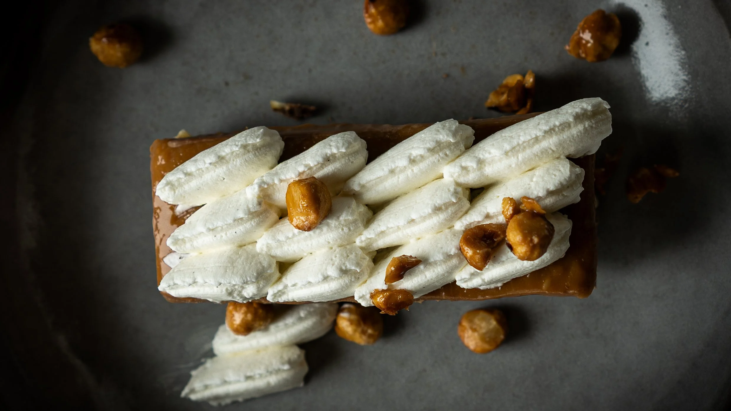 A chocolate dessert topped with whipped cream and caramelized nuts on a gray surface.