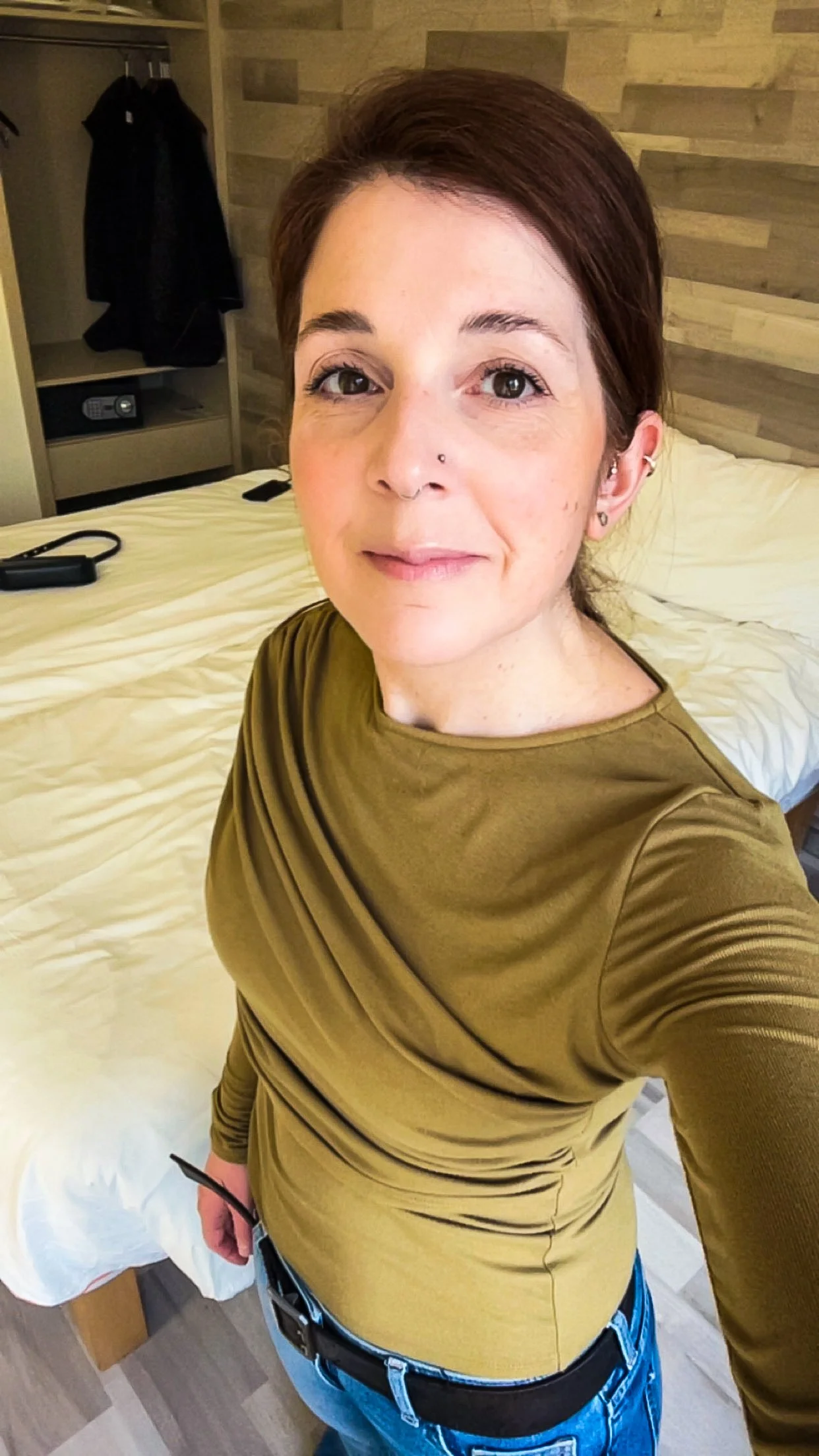 A woman taking a selfie in a hotel room with a bed in the background.